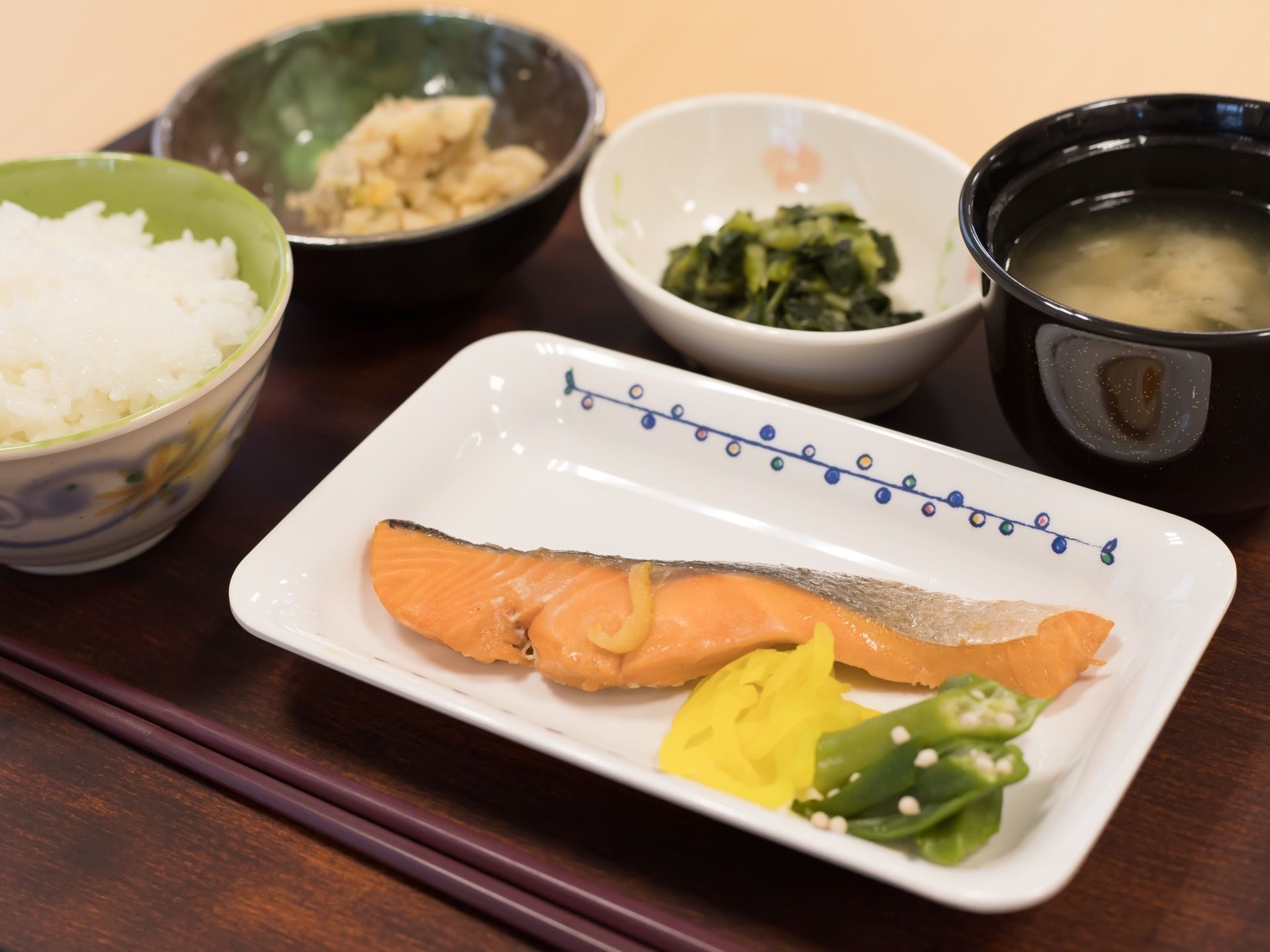 トレイに、ご飯と汁物を含めて5品が用意されている。鮭の切り身と小鉢があり、必要な量が確保されている。