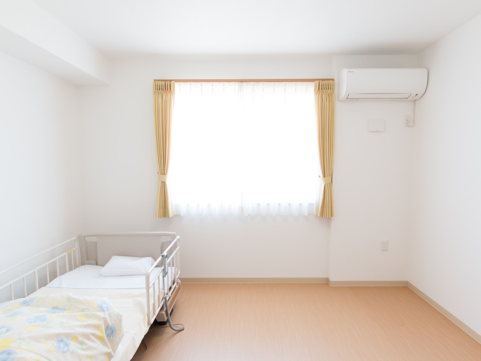 フローリングの室内に、ベッドが用意されている。窓が大きく、カーテンで陽射しの調節が可能になっている。車椅子でも問題ない広さになっている。