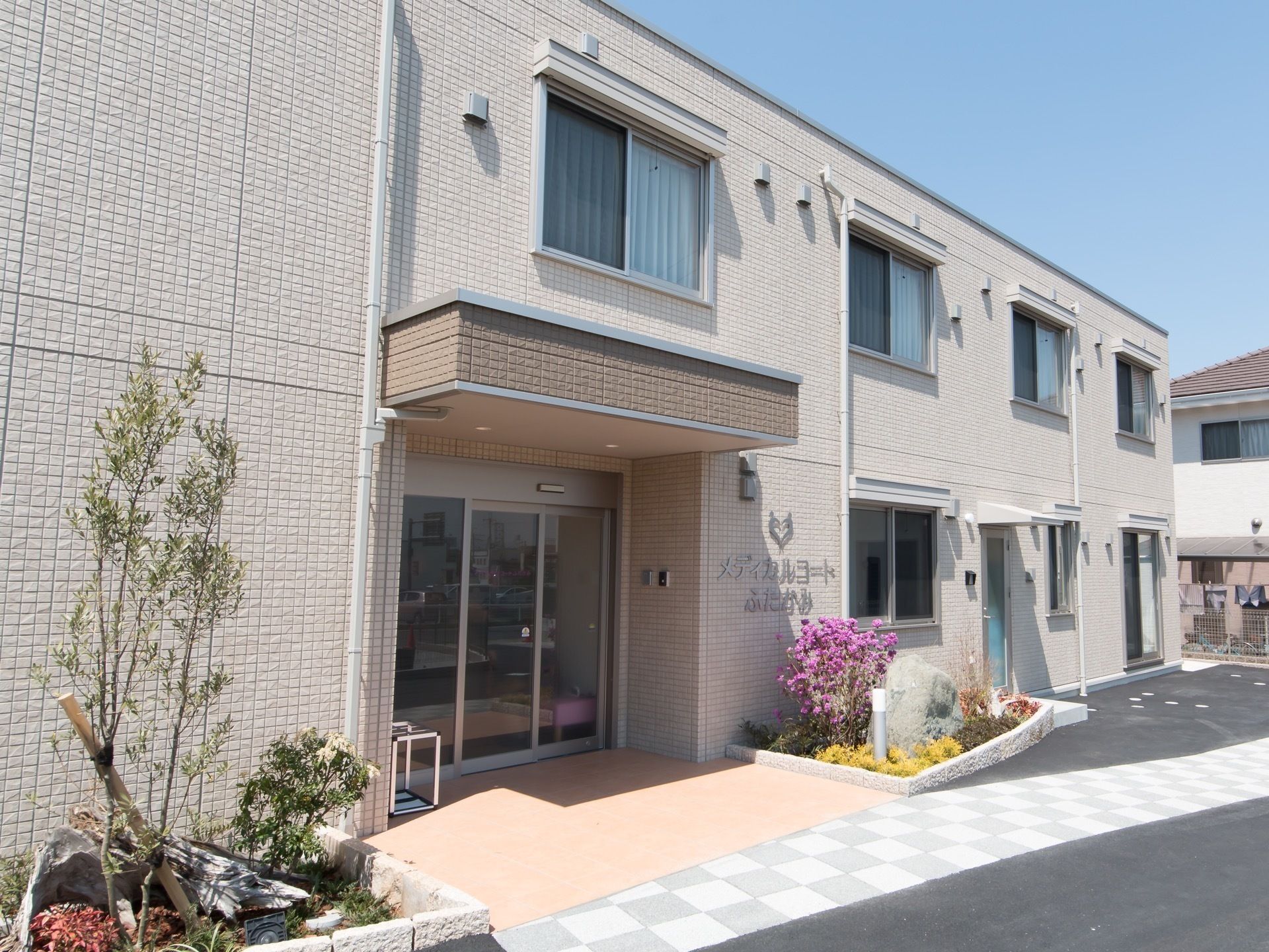 両脇に木や花が植えられている花壇がある屋根付きのエントランス