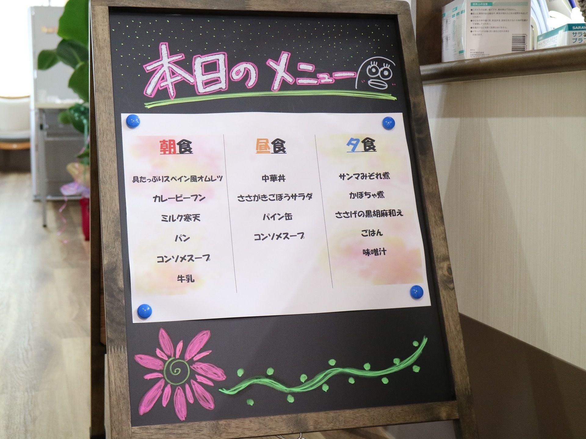 折りたたみ式の黒板ボードに本日のメニューと題し、毎食のメニューを紙に記載し、貼り付けて設置されている。