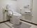 白を基調とした清潔感ある、未使用状態のトイレである。壁には手すりや緊急呼び出しブザーがある。