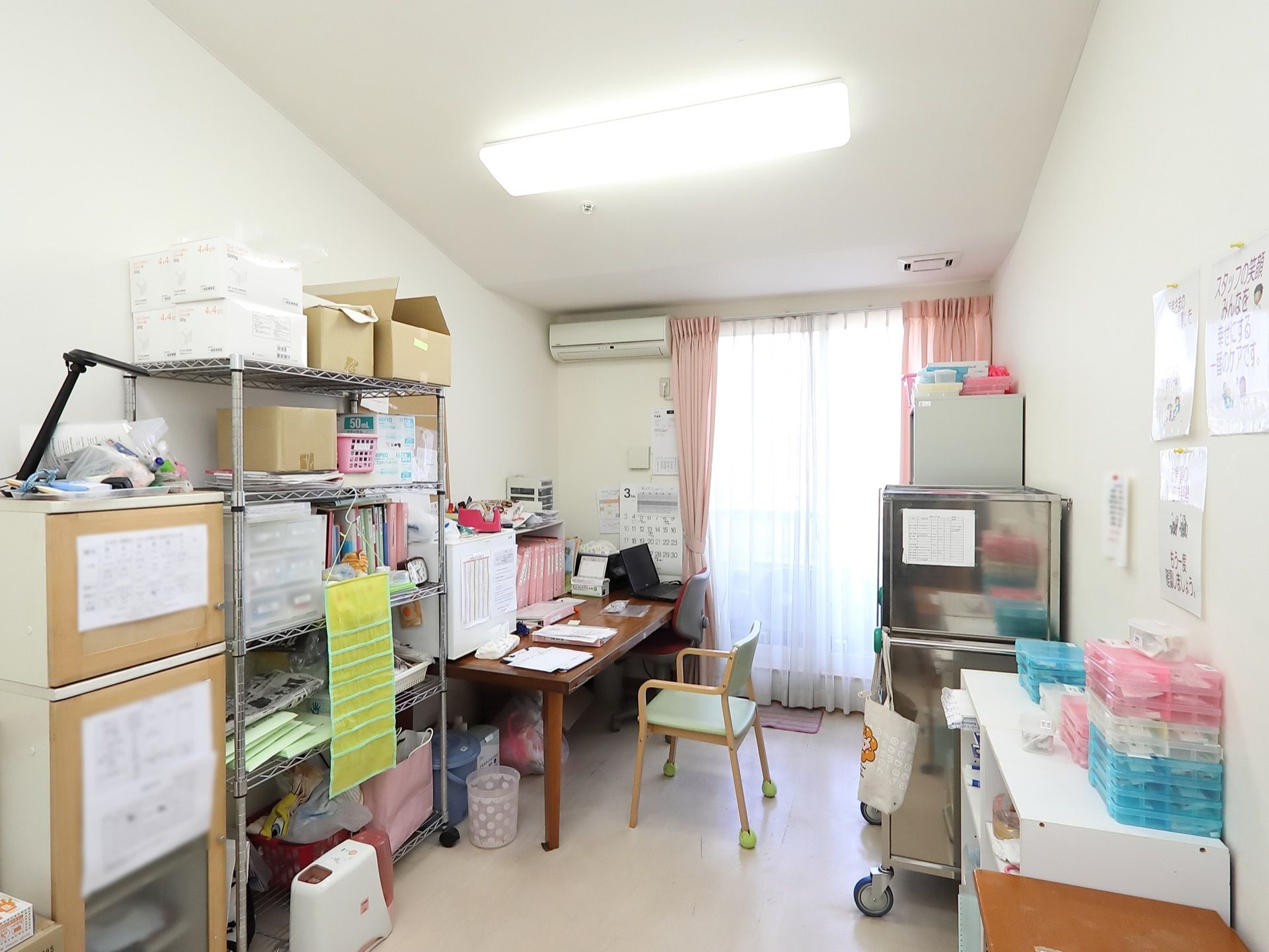 スタッフが作業する部屋の一角である。白色で統一された部屋には、テーブルや棚があり、所狭しと資料が並べられている。