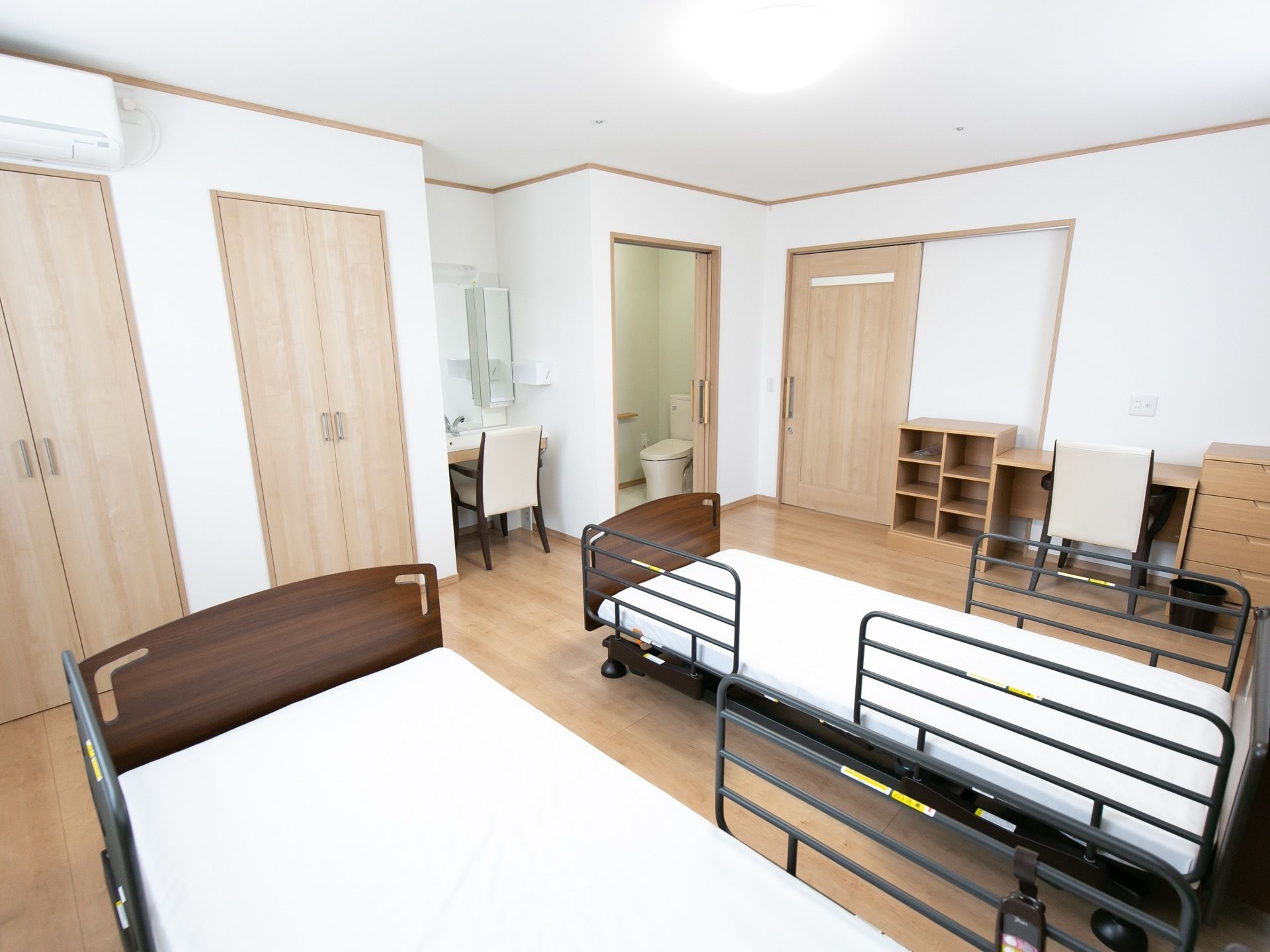 夫婦部屋で、電動ベッドとクローゼットがそれぞれ２つずつ用意されている。居室のドアの近くには、オープンラックやデスクなどが置かれている。
