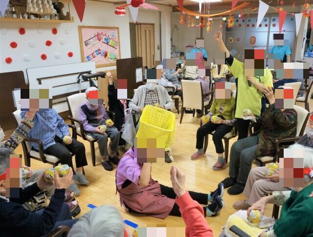 机の上に、新聞紙と花が沢山置かれている。机には高齢者が座ってフラワーアレンジメントをしている