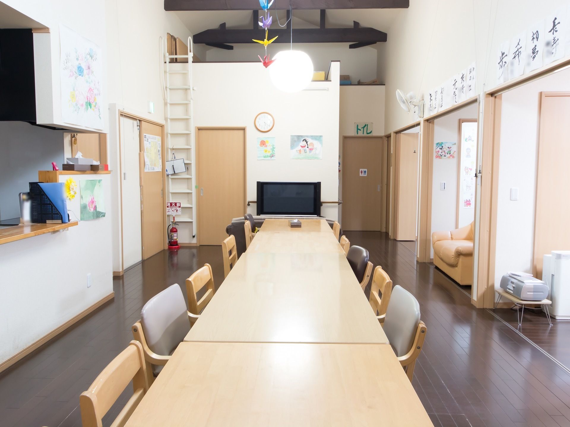 食堂の壁に入居者様の書道の作品が貼られている。天井からは丸いモダンな照明が下がり、その前に折り紙の飾りがある。