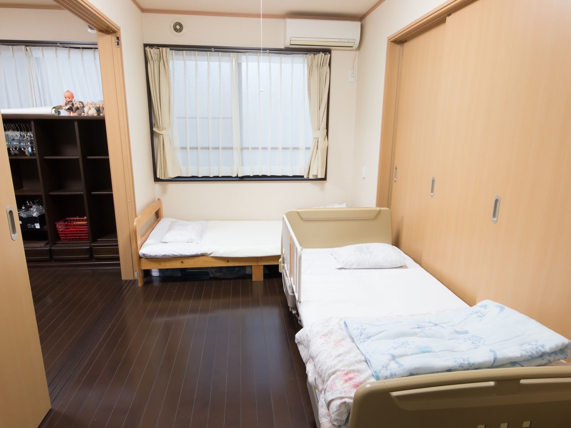 居室は二間続きとなっていて、右側の部屋にベッドが２台直角に配置されている。窓の上にエアコンが取りつけられている。