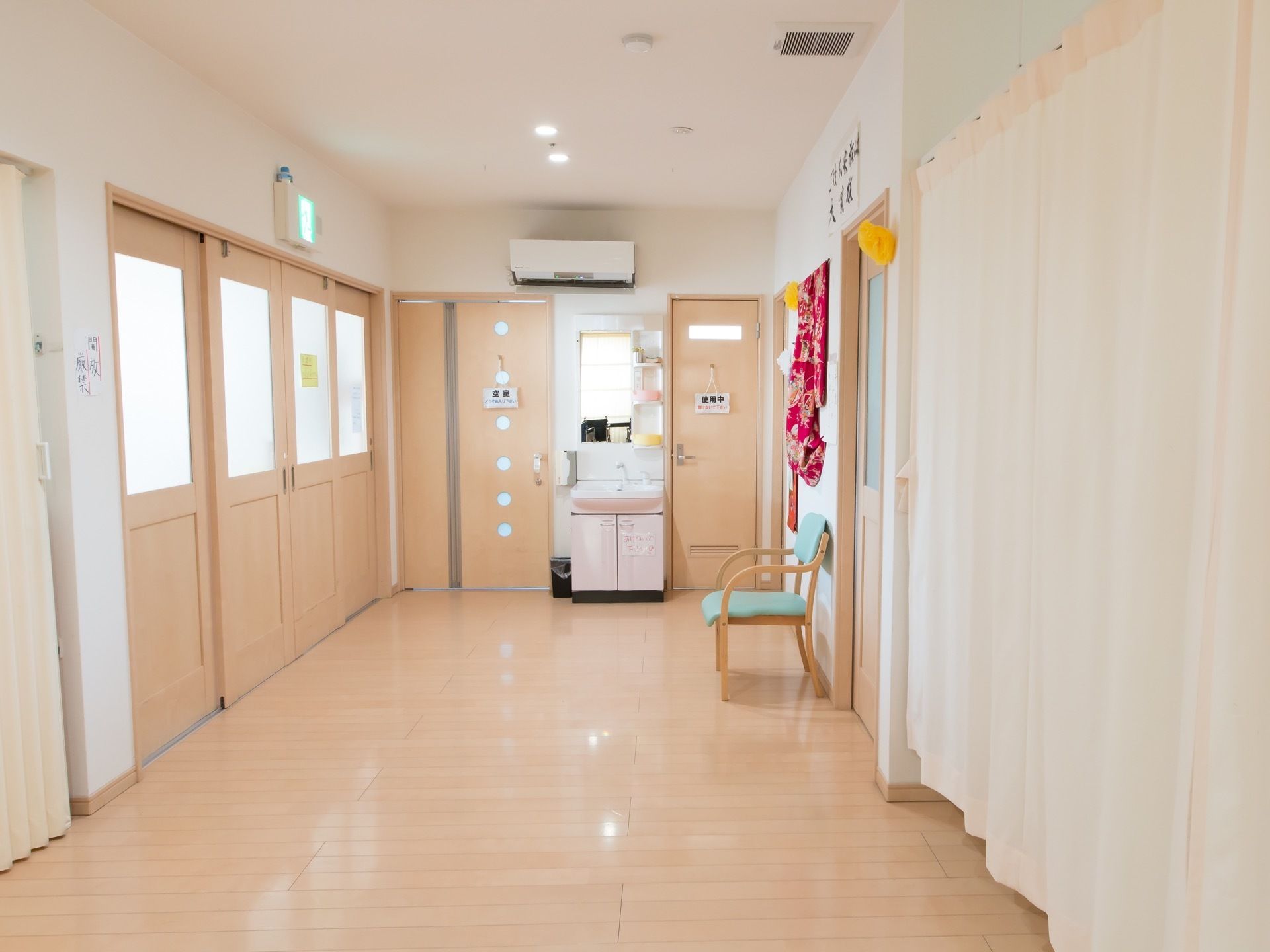 明るいベージュの床とドアに囲まれた通路がある。玄関先へ続いている大きなドアがある。正面にはトイレのドアがあり、洗面台が置かれている。