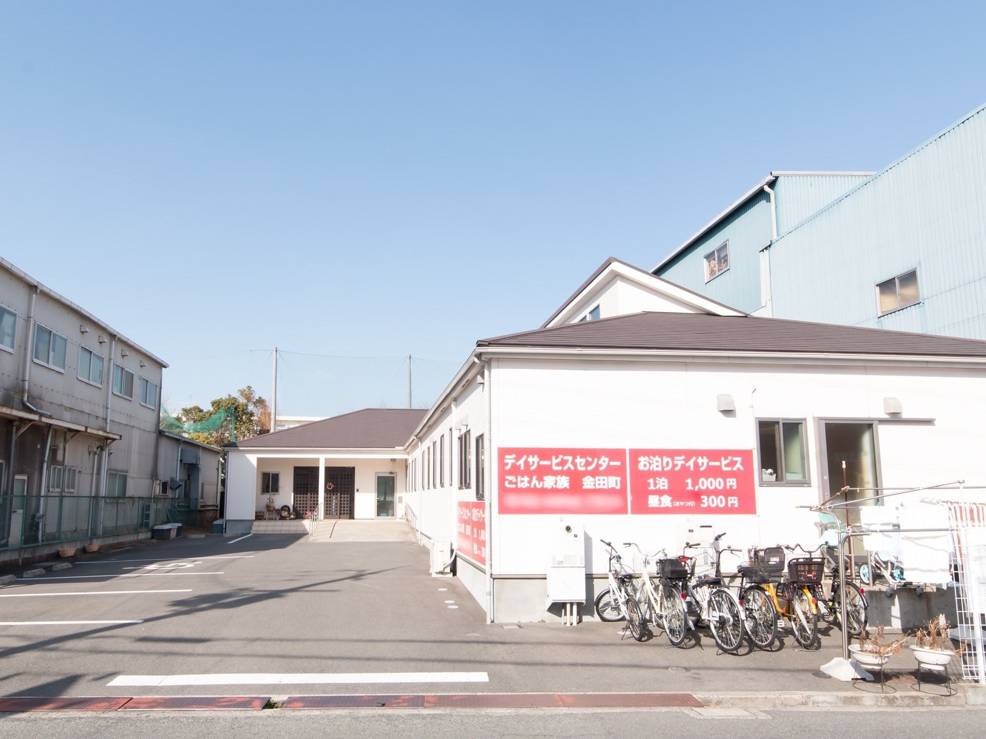 L字型の平屋建ての大きな建物がある。車道に面した位置に駐輪場があり、自転車がたくさん停められている。敷地内には駐車場がある。