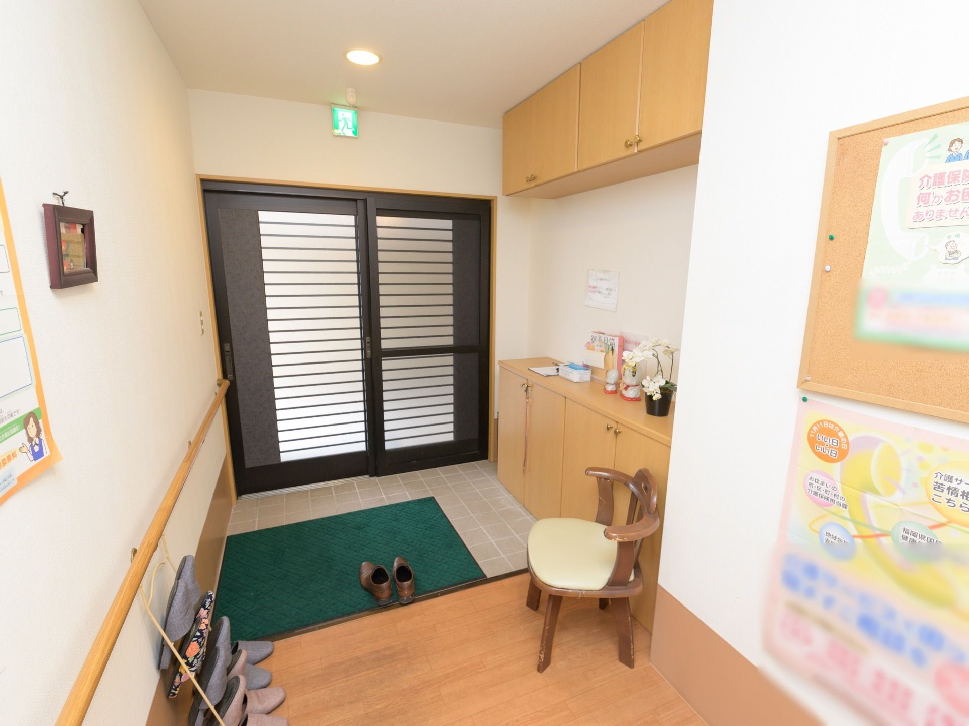 家庭的な雰囲気の玄関である。壁際に靴箱が設置されており、スリッパラックと椅子が置かれている。玄関は引き戸になっている。