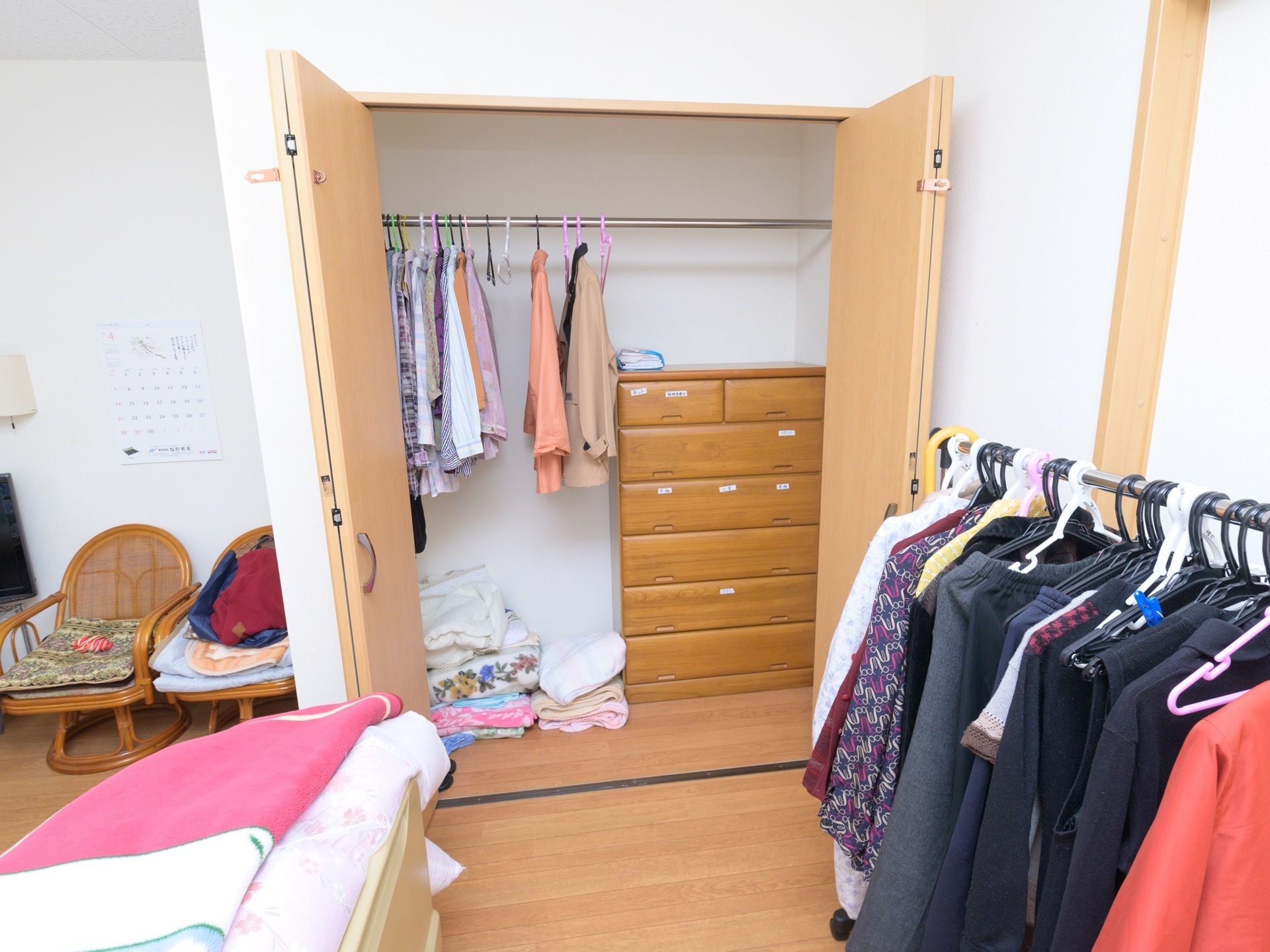居室に完備されている両開き式の収納クローゼットである。扉は開かれ、整理ダンスや洋服がハンガーバーに掛けられているのが見える。