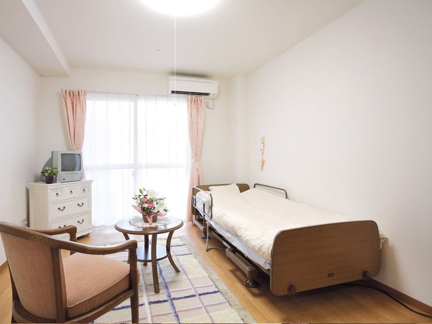 大きな窓が付いたフローリングの居室にはエアコンやベッドといった家具家電が置かれている。