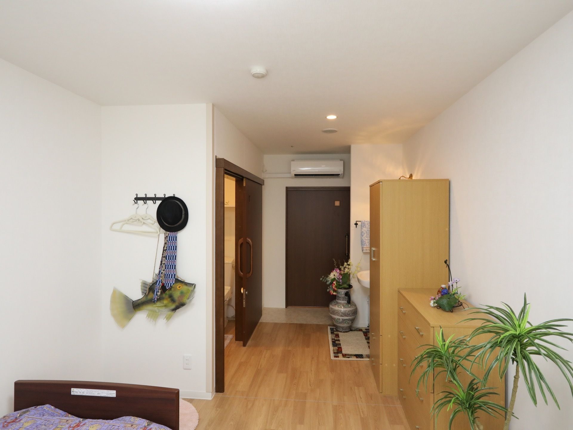 居室入口の扉の上の壁にエアコンが設置されている。入口を入ってすぐの所に、トイレの扉があり、その反対側に洗面台がある。
