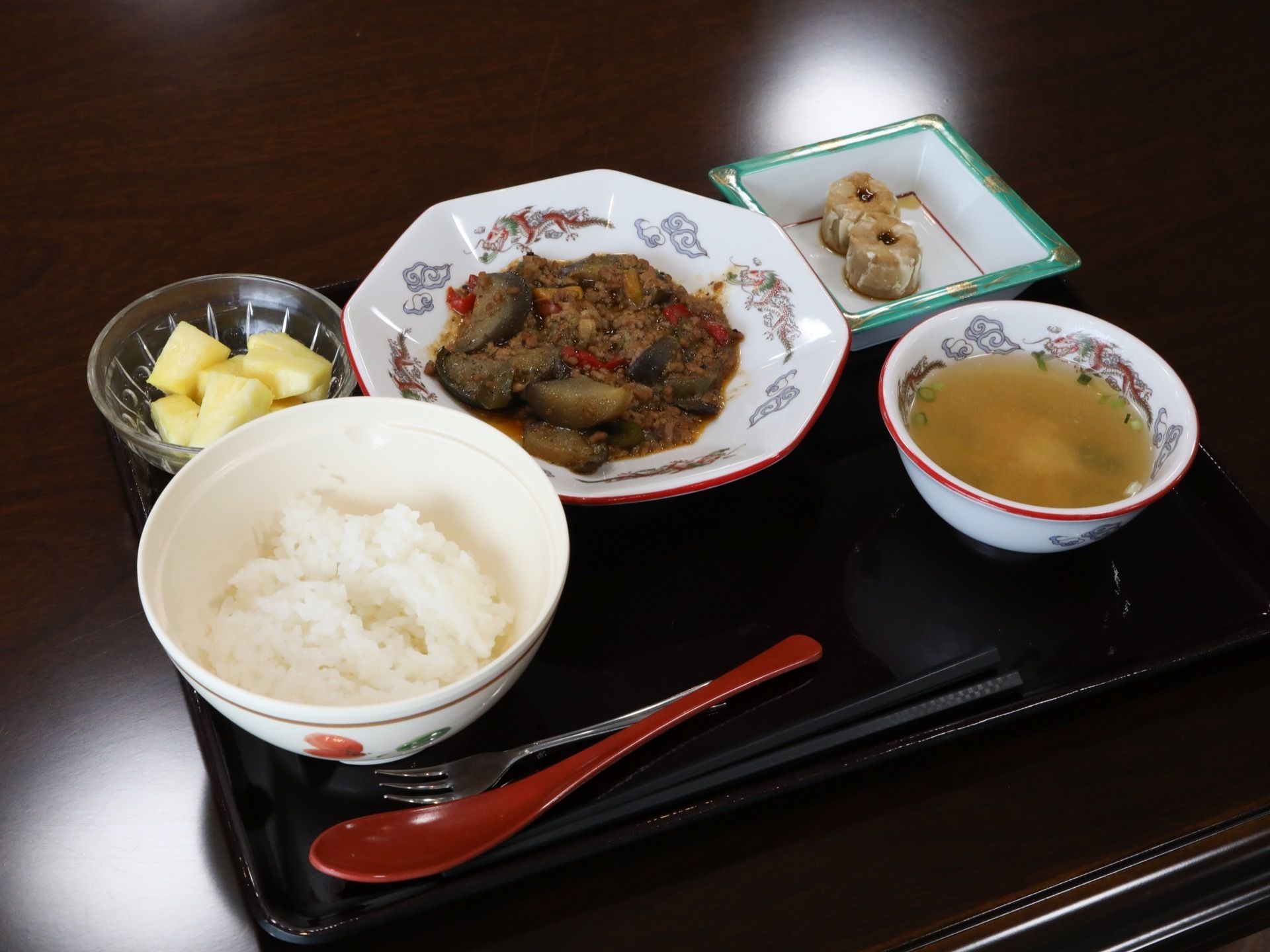 中華風の食事である。中国をイメージさせる食器に、ご飯、スープ、餃子やメインのおかずが盛られている。赤色のレンゲが置かれている。