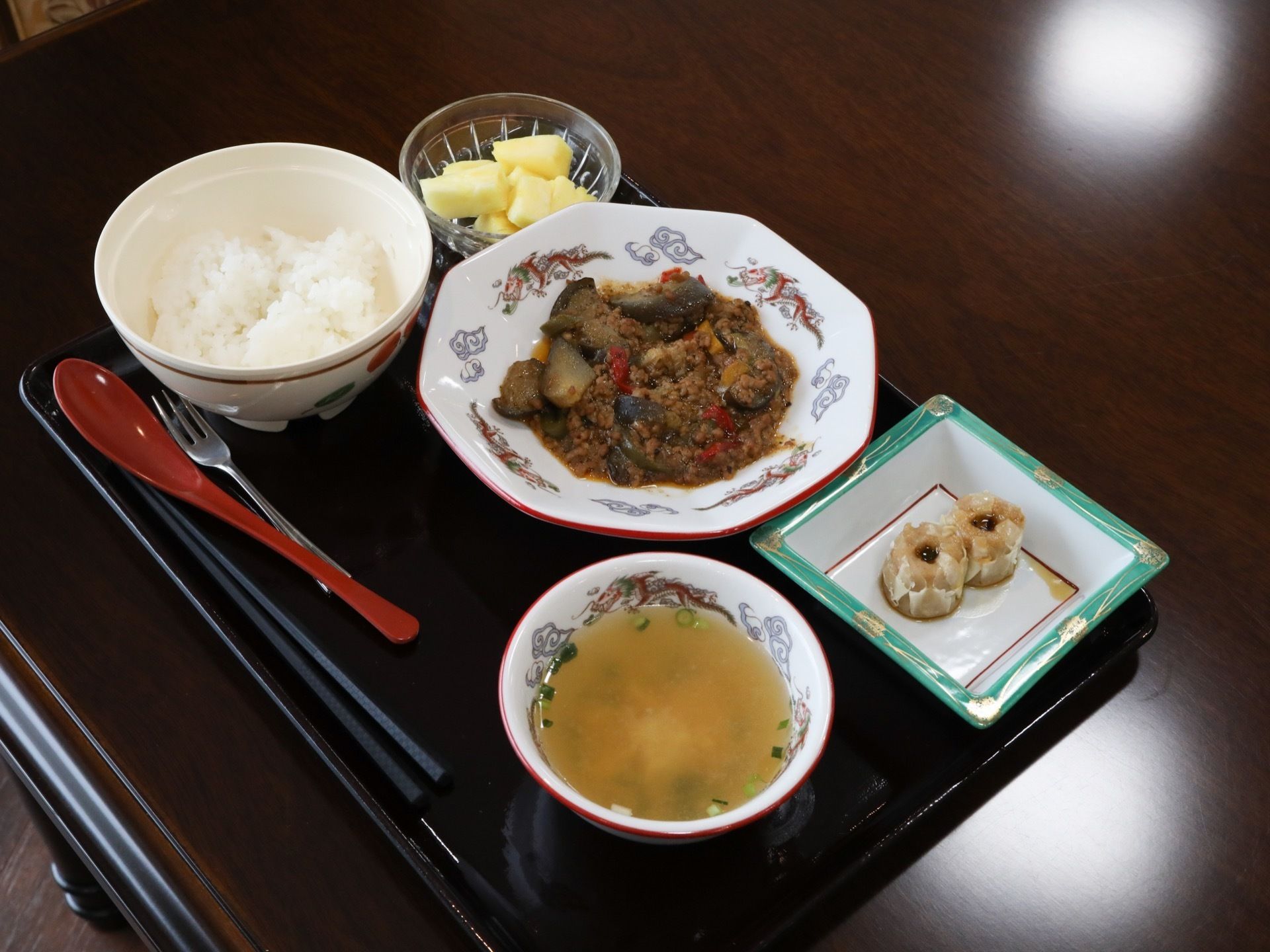 テーブルの上に置かれた黒いプレートに、食事が載っている。透明な小鉢に入ったフルーツが左奥に置かれている。