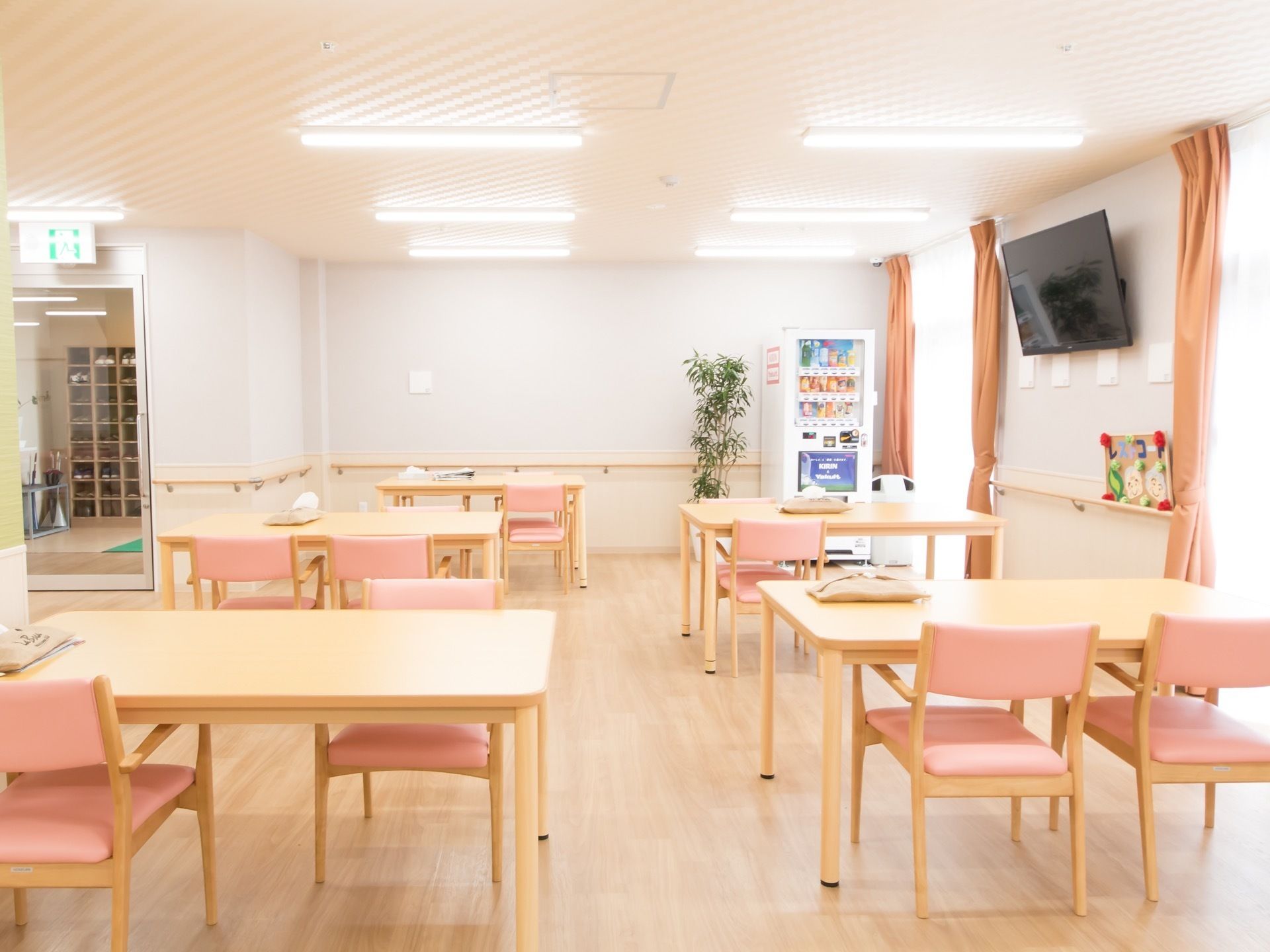 椅子とテーブルがゆとりをもって並べられている。自動販売機が設置されている。壁にテレビが備えつけられている。