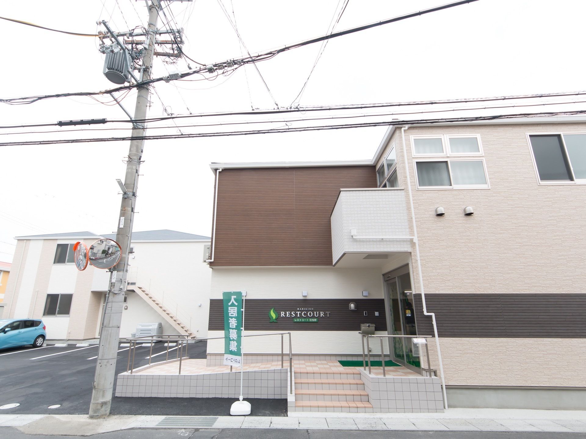 道路に面している。広い駐車場が併設されている。ミラーのついた電柱が立っている。２階建ての建造物である。