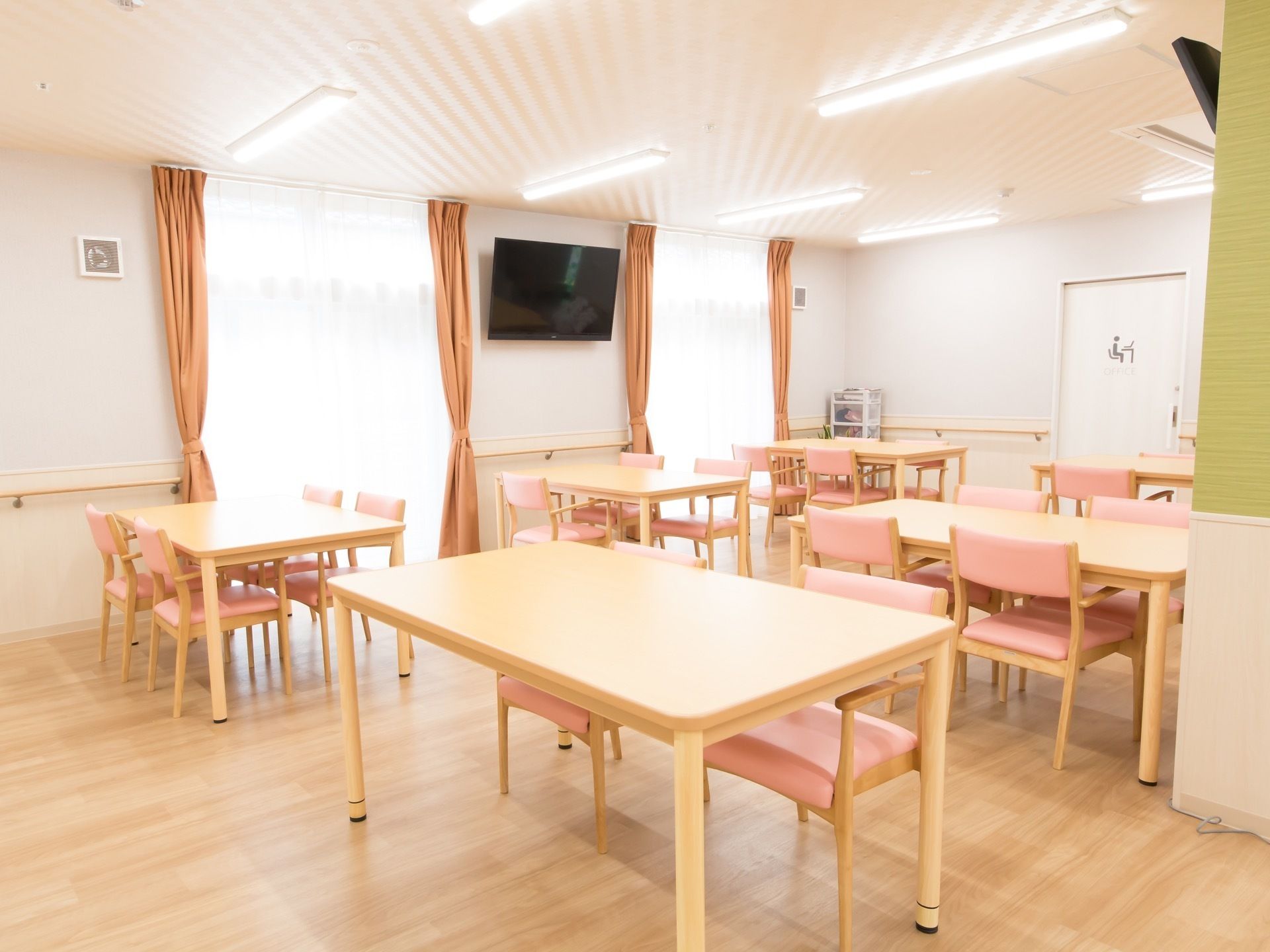 食堂には４人掛けのテーブルとピンク色の椅子が複数設置されている。窓の間の壁に大きなテレビが掛けられている。