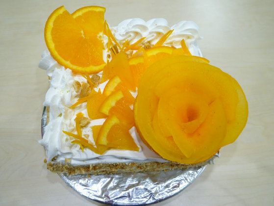 オレンジが飾られた生クリームたっぷりのケーキ。アルミの皿からあふれそう。