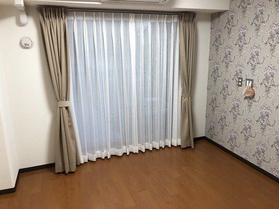 大きな窓にはベージュのカーテンとレースカーテンが付き、壁には緊急通報装置が設置されている。