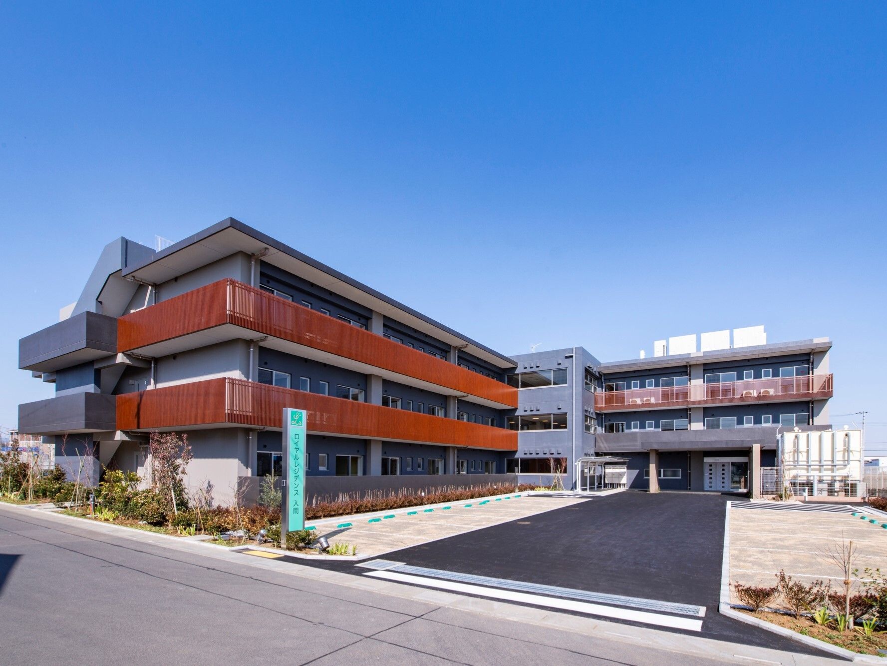 ３階建ての建物。各フロアにベランダが設置され、玄関には屋根が付いている。広い駐車スペースや菜園もある。
