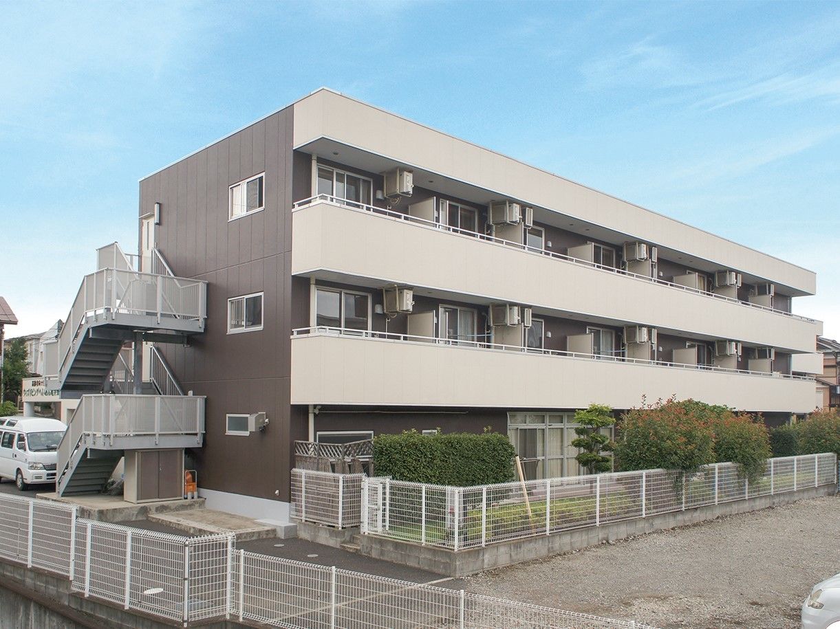茶色を基調とした壁の建物。建物は3階建てで、左側には非常階段がある