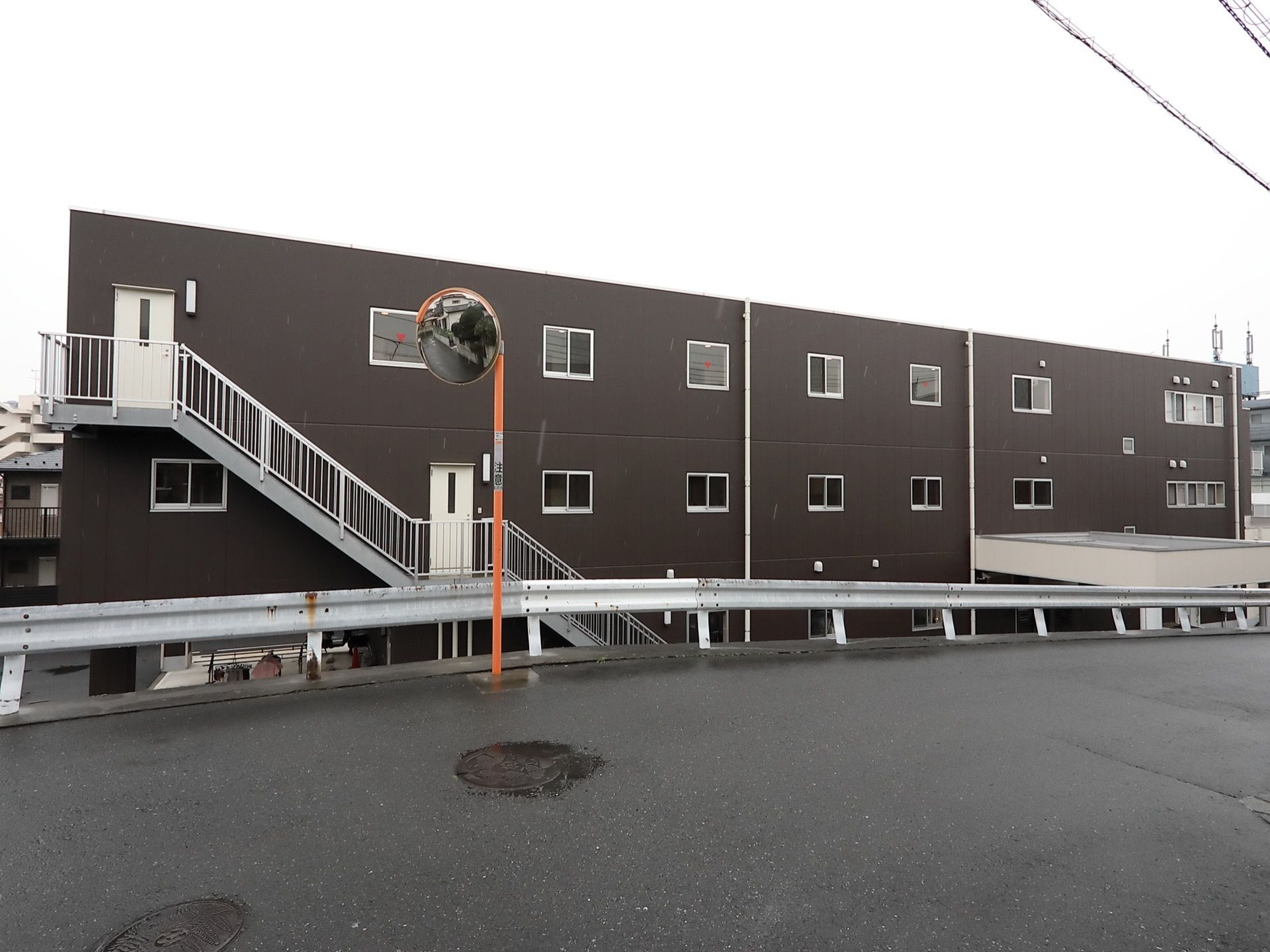 道路から一段低くなっている敷地に建っている、シンプルな外観の施設である。手すりがついた非常階段が設置されている。