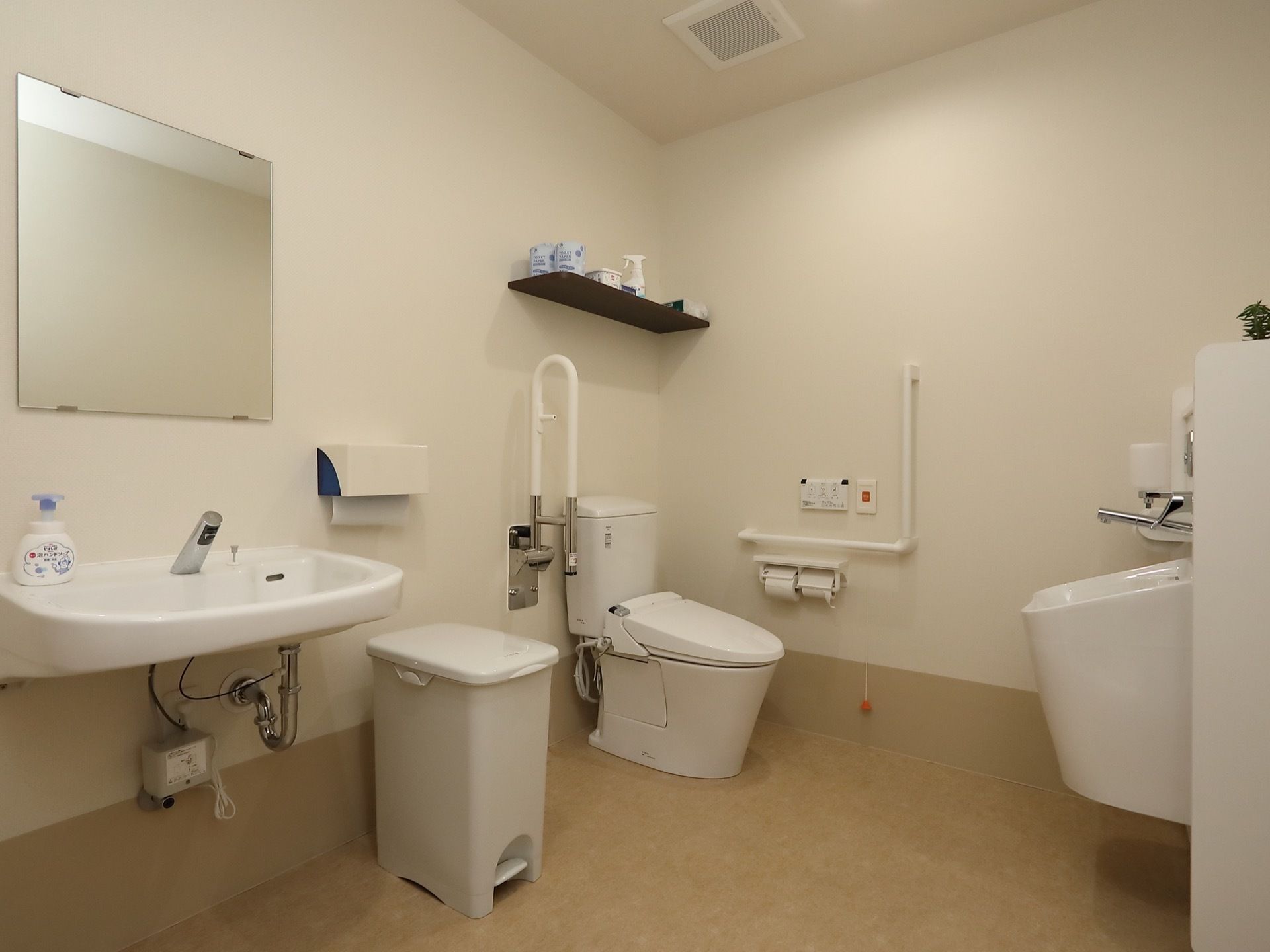 広いトイレスペースに洋式便器とオストメイト対応の設備を設置している。壁にはＬ字型と折り畳み式の手すりを取りつけている。