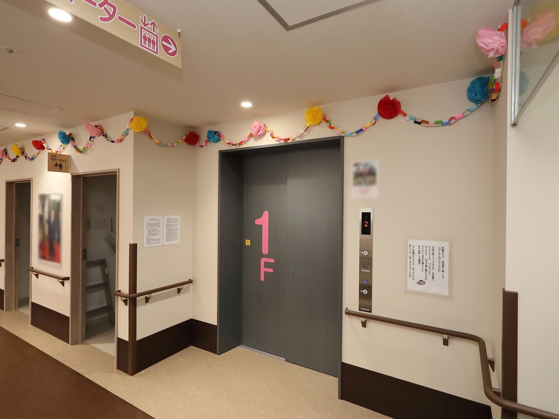 エレベーター前の床はフラットで、扉前を明るい色に変えている。両側の壁には手すりを設置し、上部に飾りつけを施している。