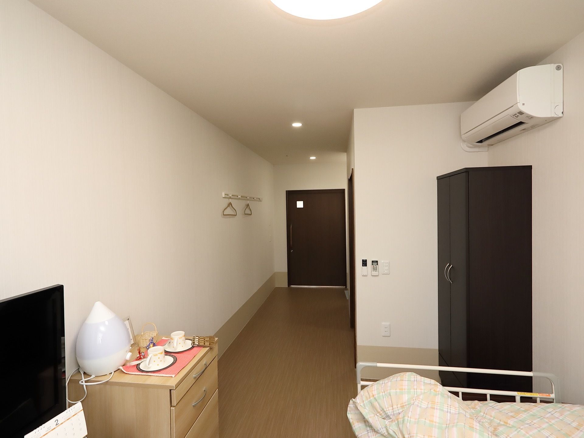 居室の床はフローリングで、壁際にクローゼットとベッドを配置している。天井には複数の照明を設置し、十分な明るさを確保している。