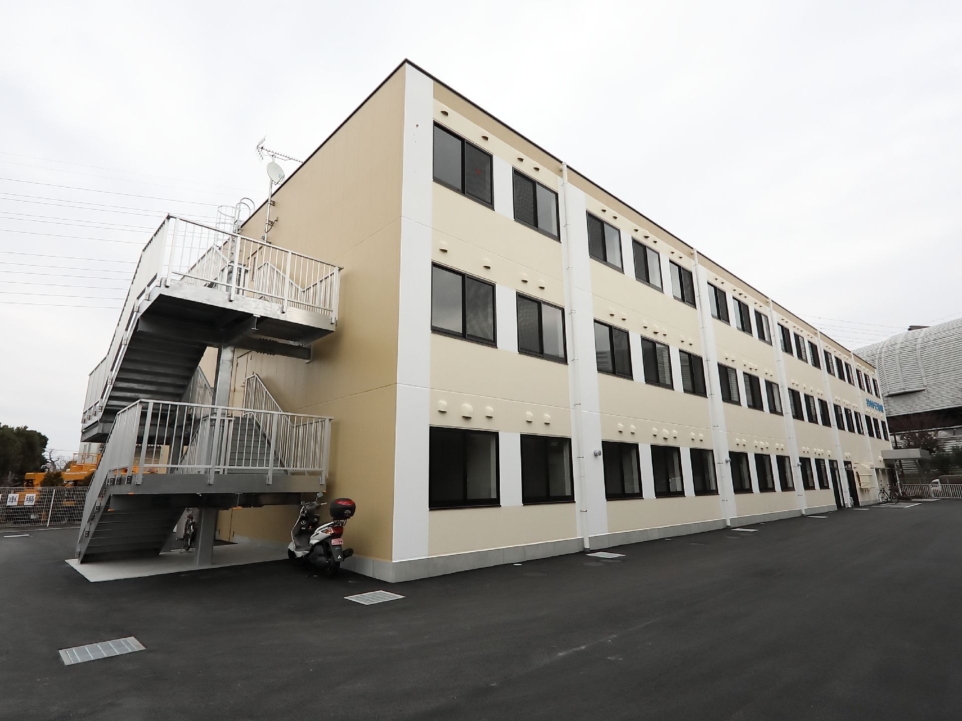 鉄骨造３階建ての建物。無駄のないシンプルなデザインの外観と広めの駐車場。