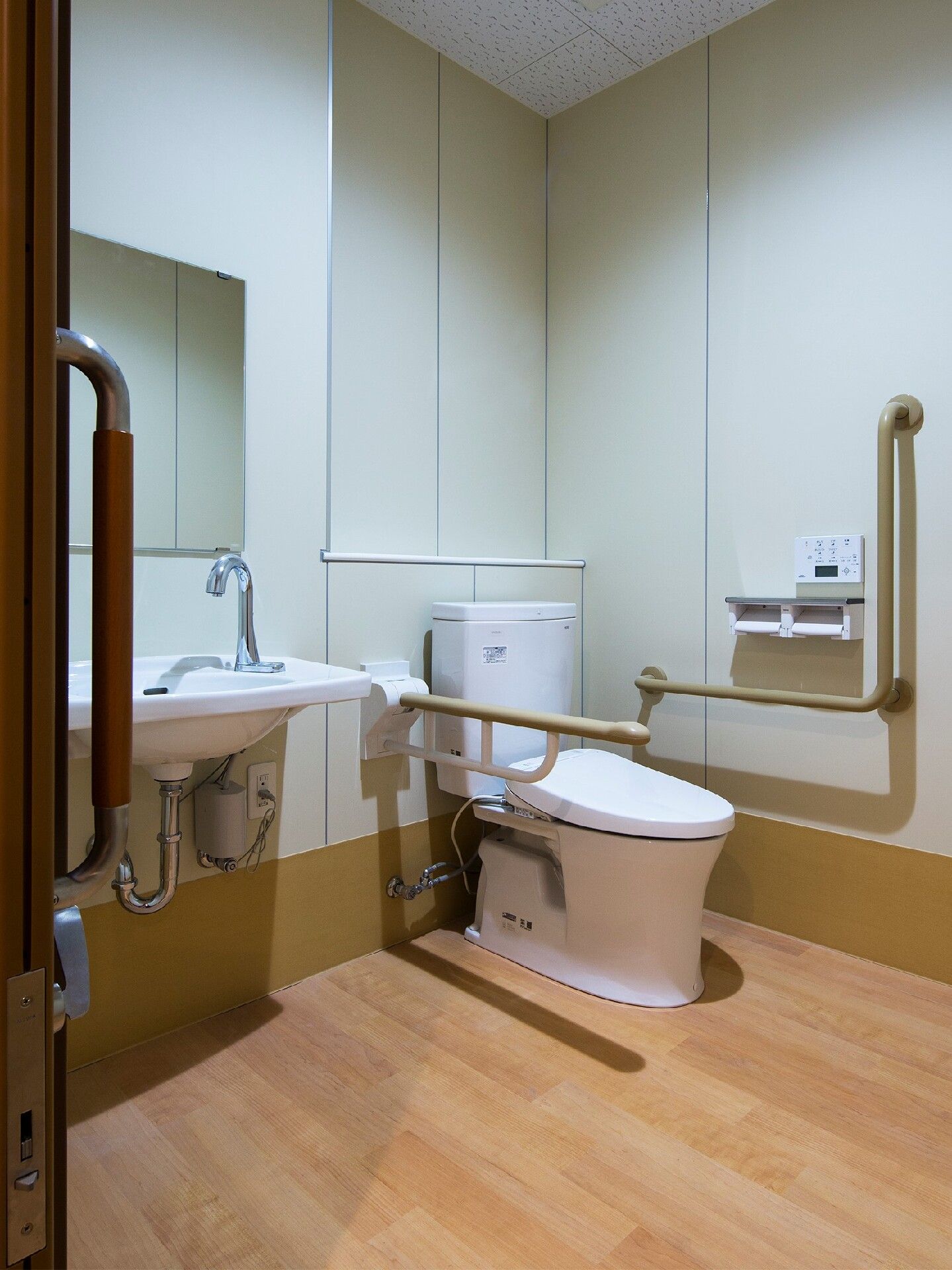 手すりが両サイドに付いたトイレには自動水栓が設置された手洗い場があり、スペースも広い。手洗い場には鏡も付いている。