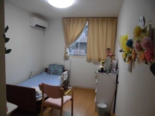 ベッドが付いたフローリングの部屋にはカーテン付きの窓やタンスがあり、あちこちに花が飾られている。