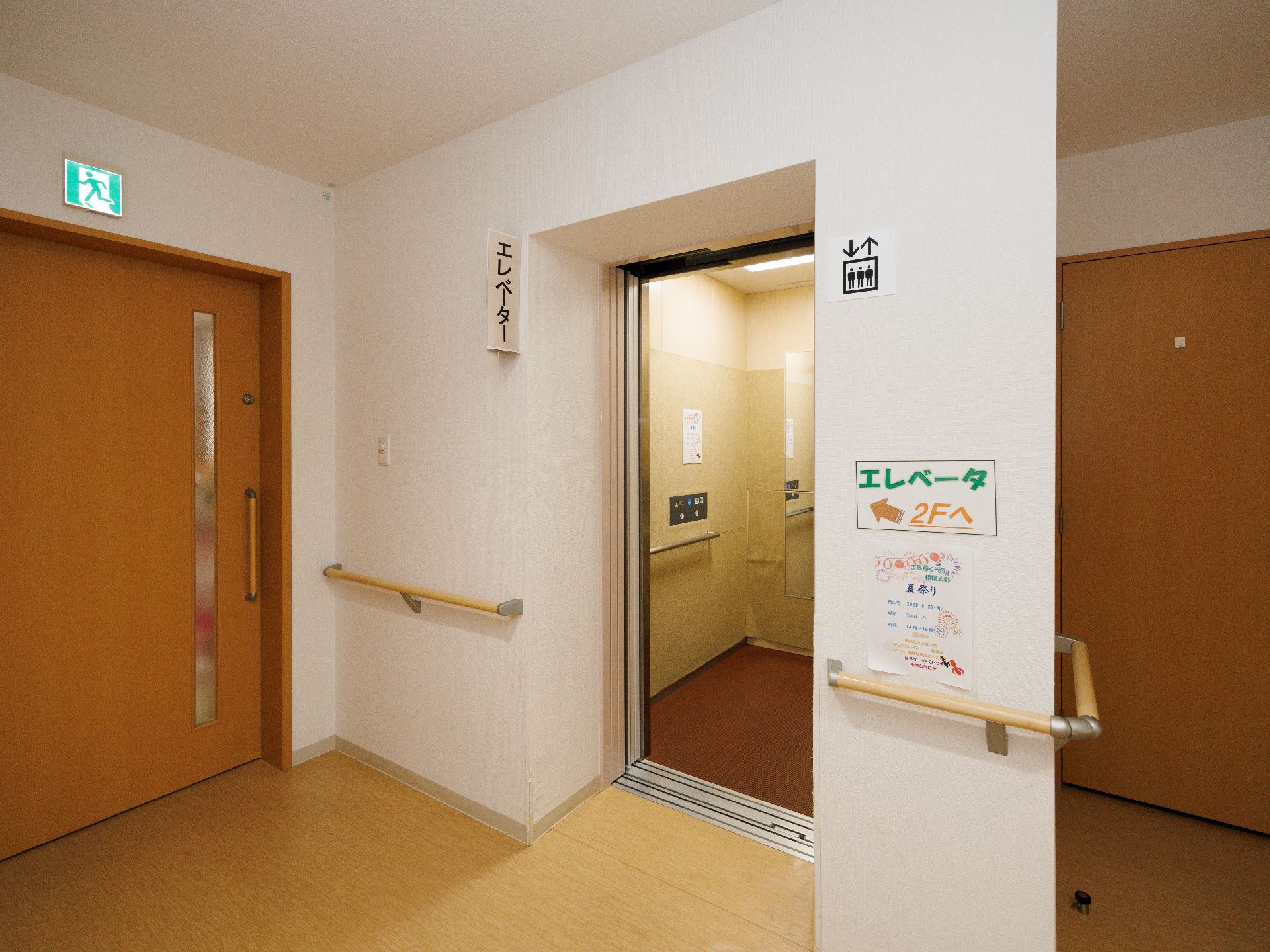 手すりのついた白い壁に配置された扉があいたエレベーター