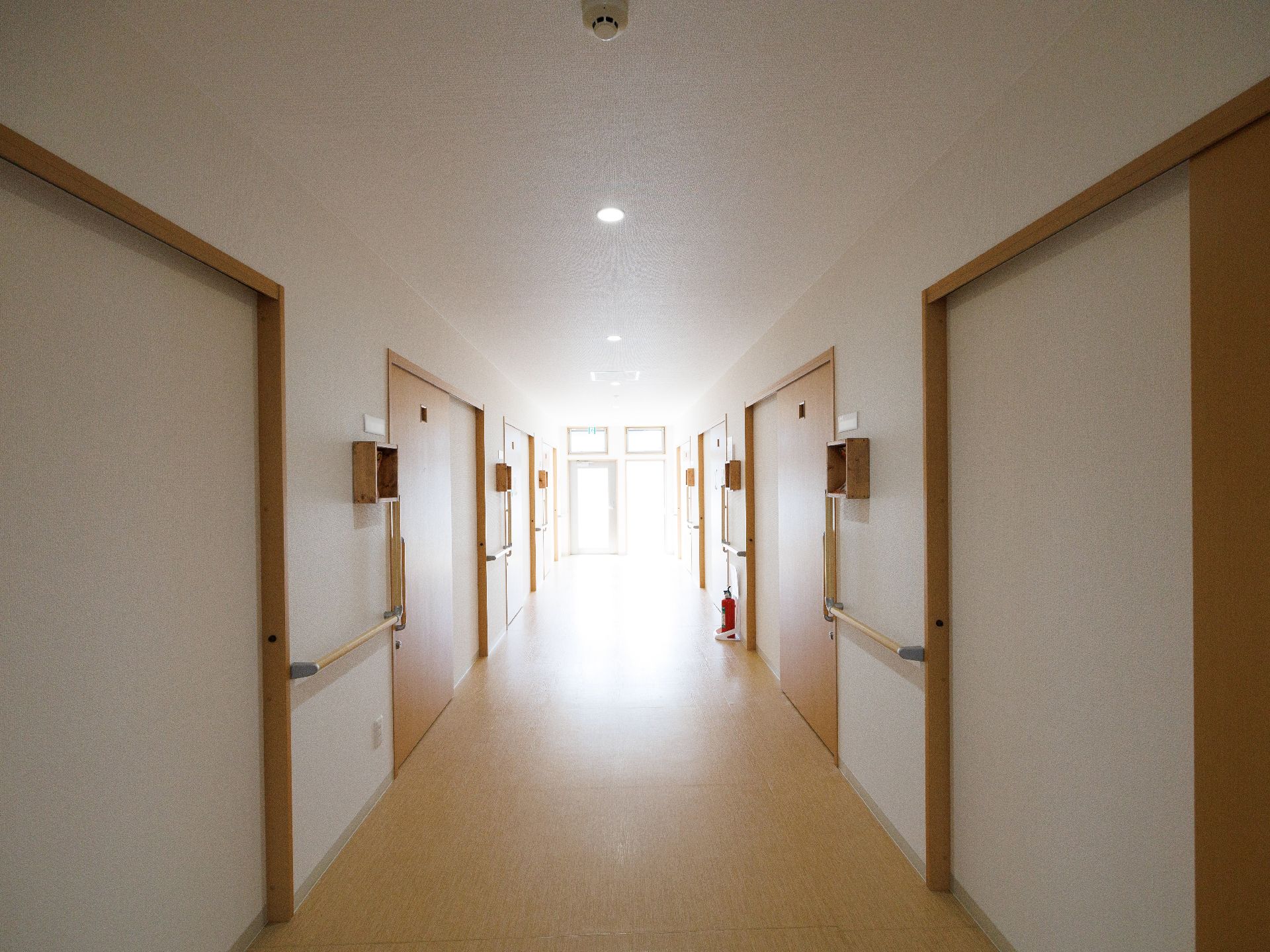 両側の白い壁に手すりと扉が付いている直線の廊下