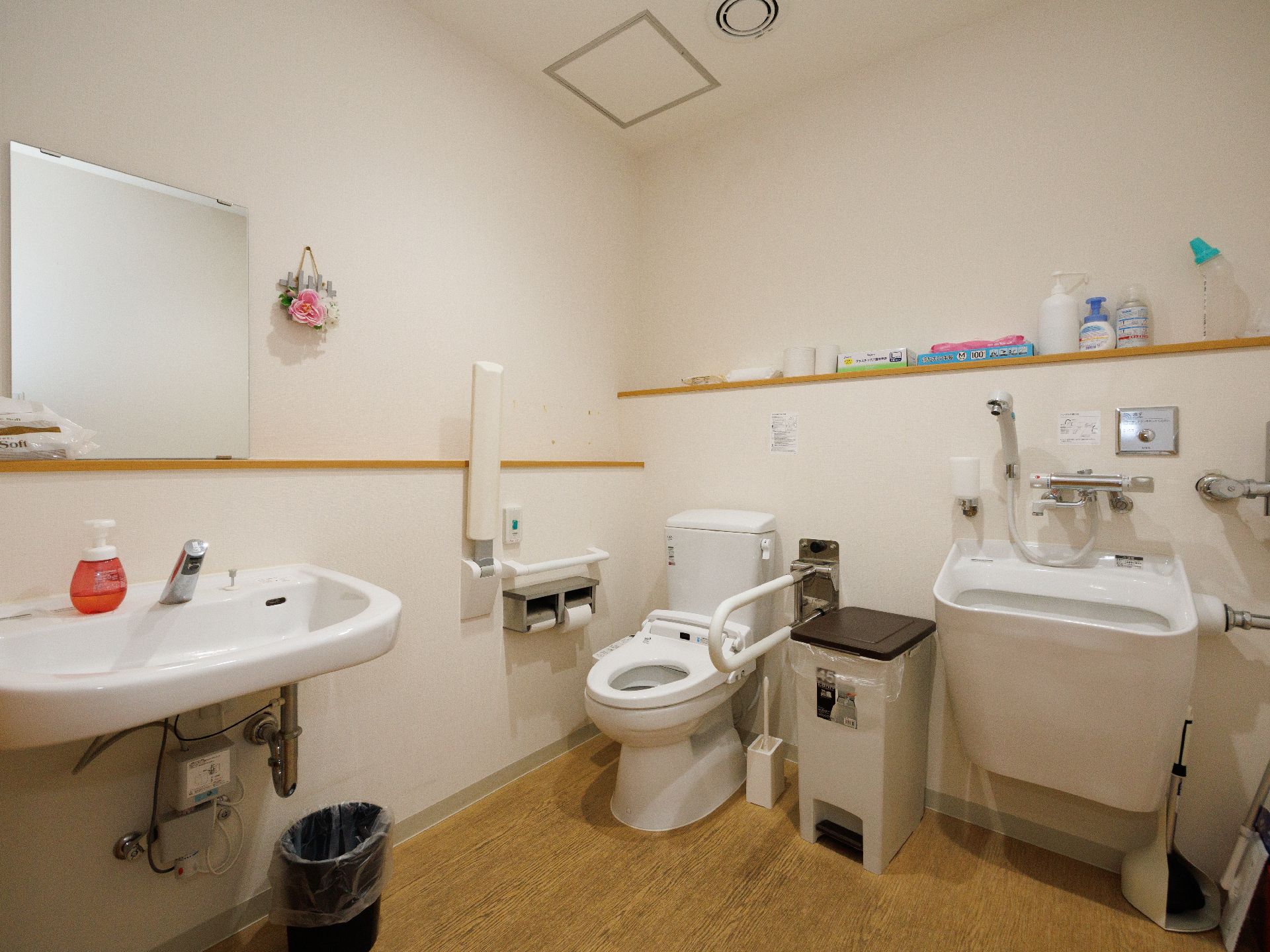 洗面台と洋式便器とオストメイトパックが角に置かれた白い壁の部屋
