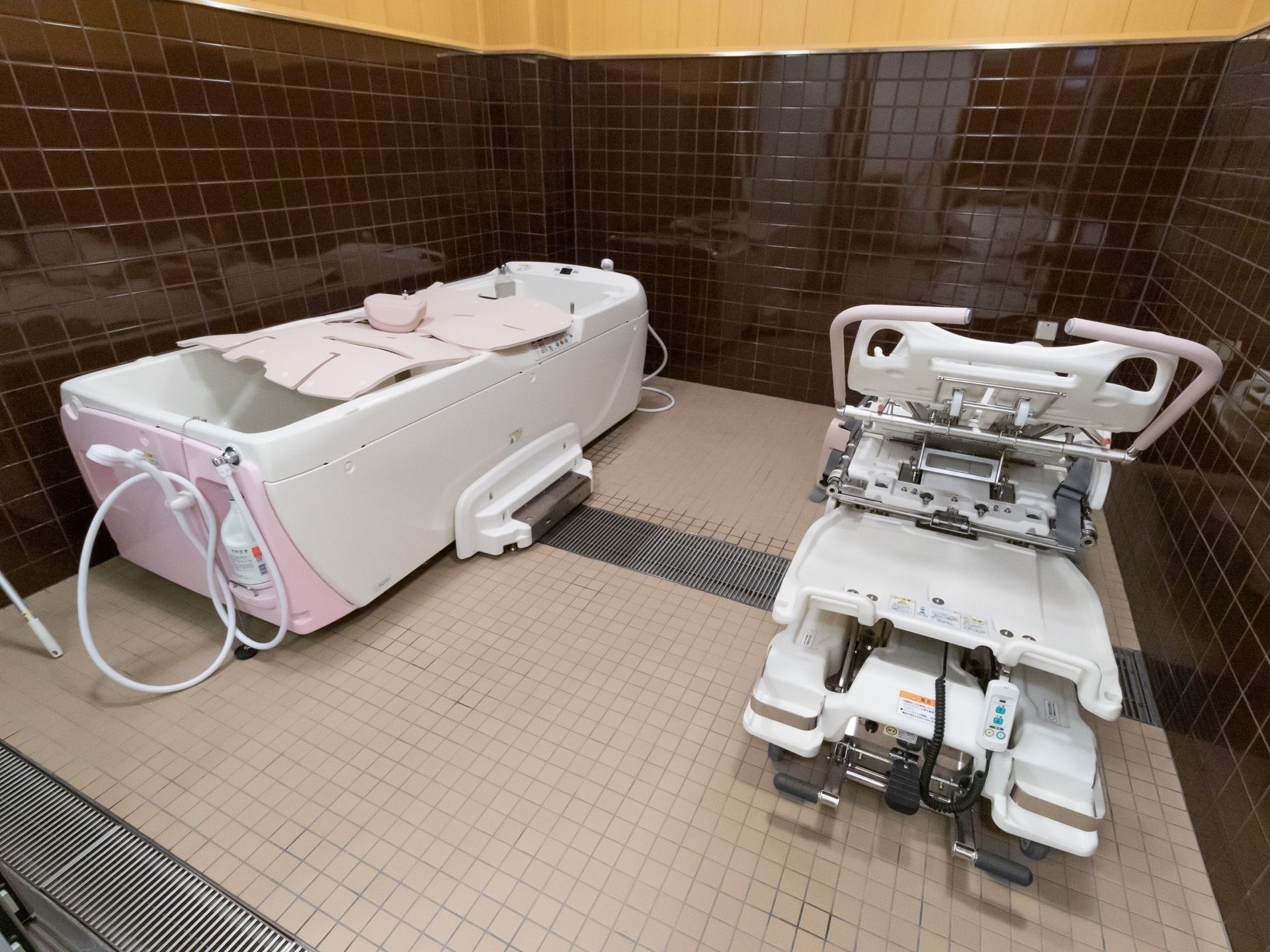 広々とした浴室があり、左手に機械浴槽、右手に専用のストレッチャーが置かれている。壁は茶色や木目調になっており、温かみがある。