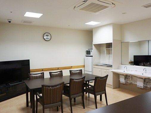 大型のテレビやIHクッキングヒーター付きのキッチン、ダイニングテーブルセットが複数置かれた共有スペース。