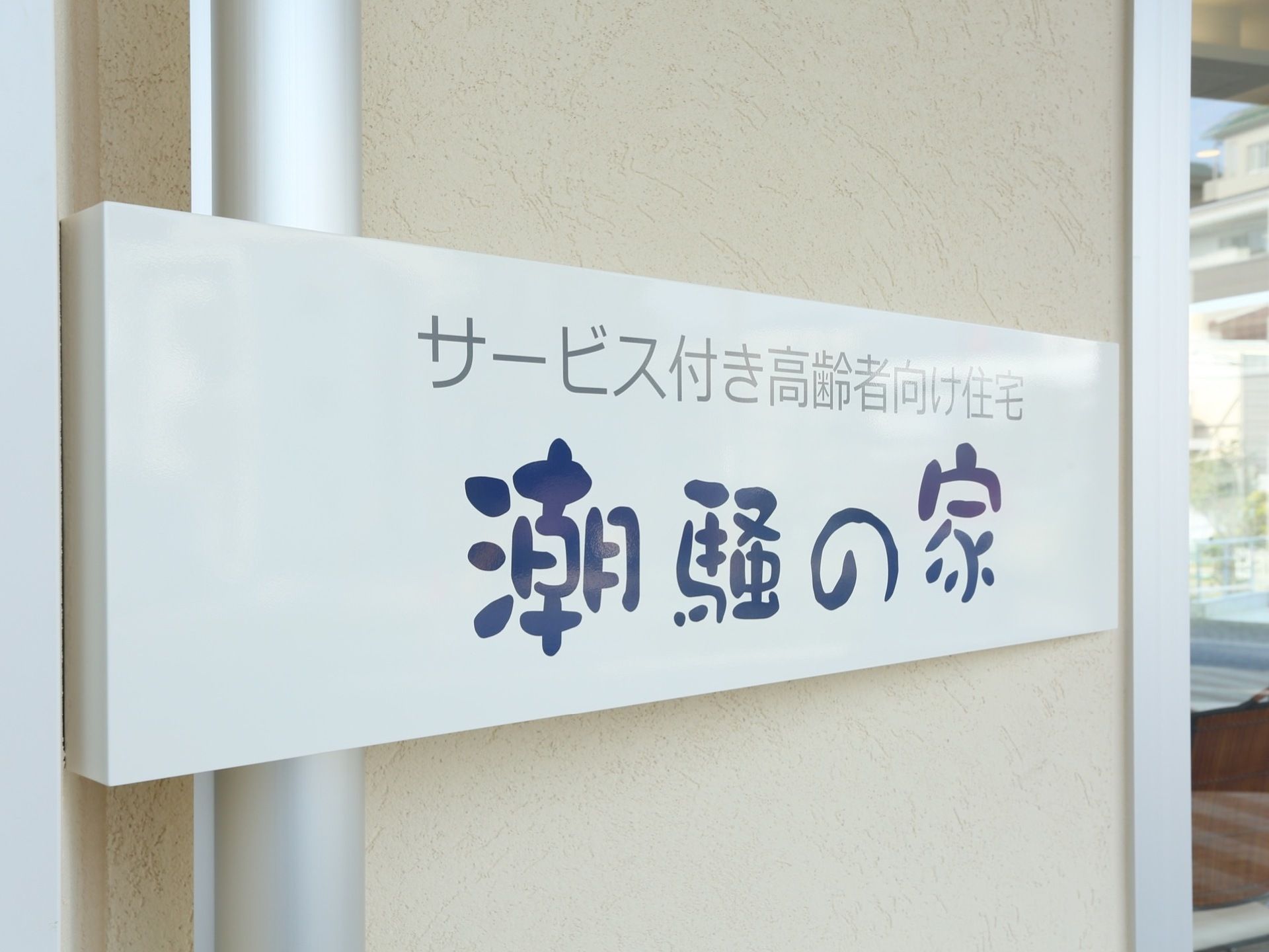 施設の玄関の壁に設置されている施設看板である。海をイメージし、また、柔らかみを持たせるため、独特なフォントで施設名が書かれている。