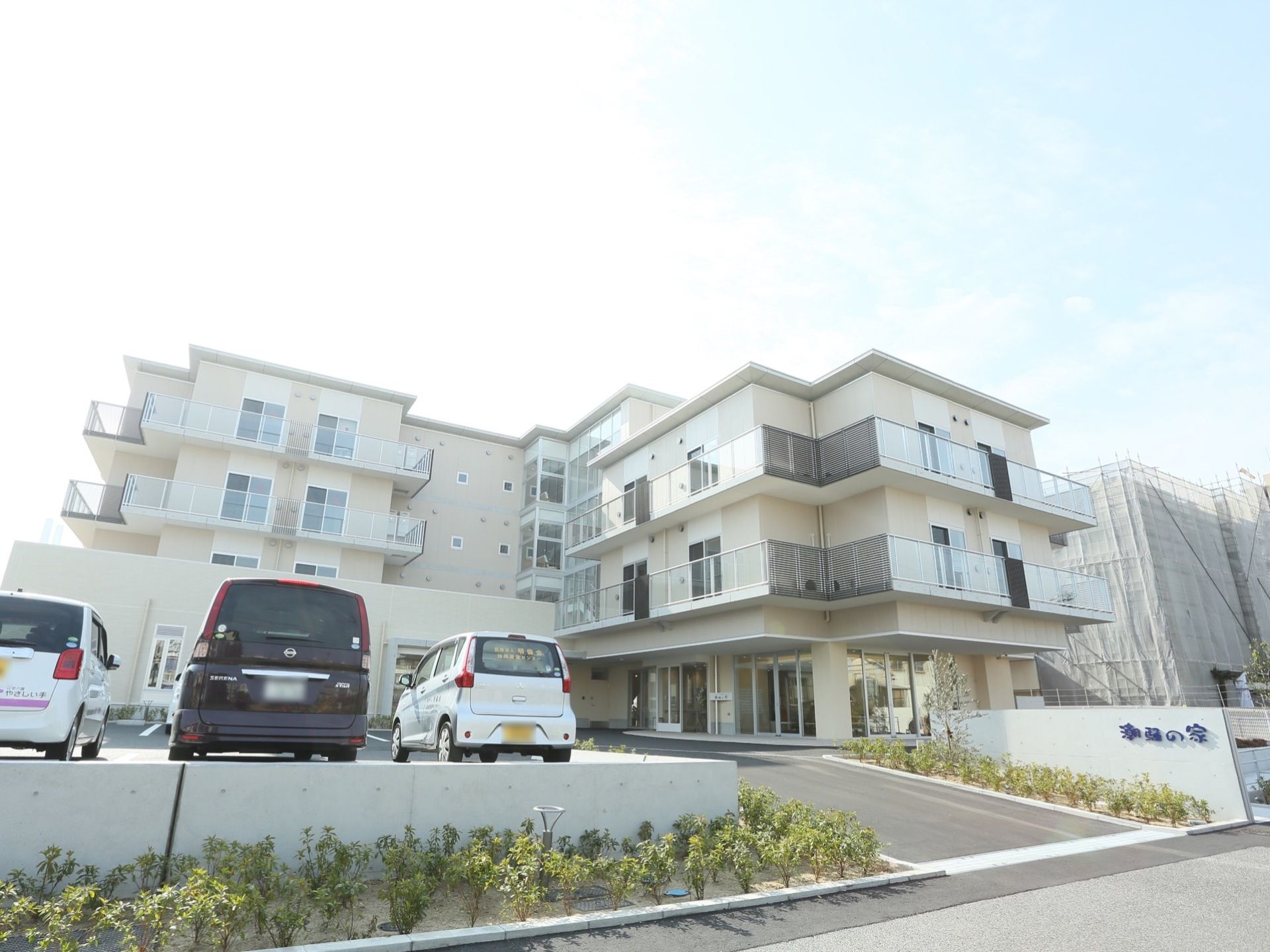 施設は白いマンションのような造りである。植え込み近くの外壁には、青色の立体文字で施設名が書かれている。