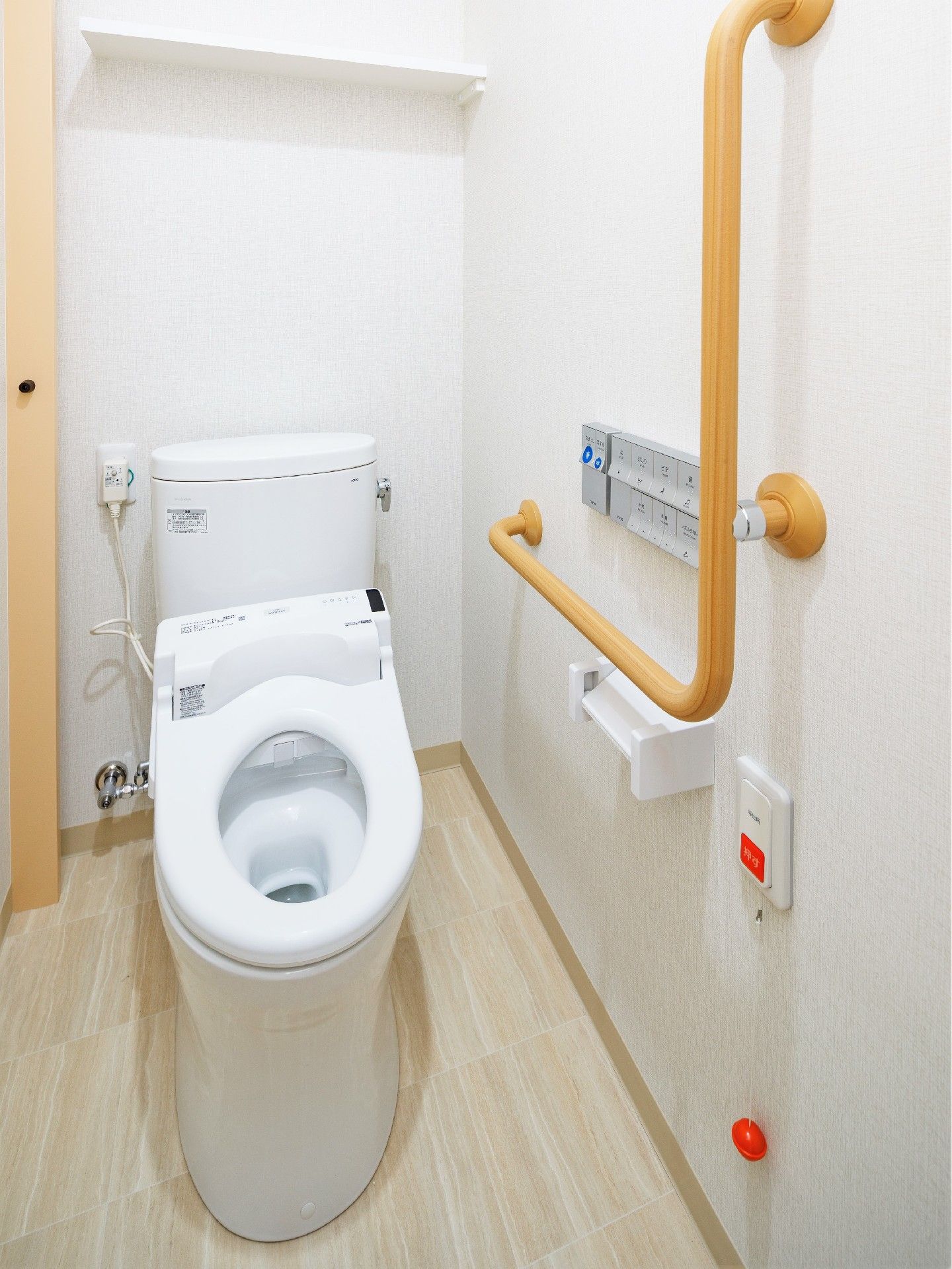 家庭的サイズのトイレに丈夫な手すりが取り付けられている様子。緊急用の呼び出しコールが付いているトイレ