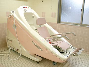 ピンクと白の機械浴が完備され、介護度の高い人にも対応している浴室。大きな窓が付いている。