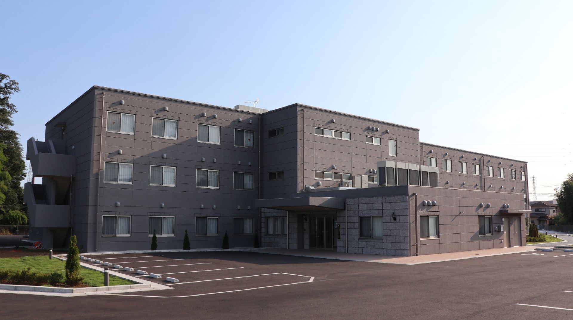 3階建ての建物はすっきりとしたスタイリッシュな外観で、玄関には屋根もあり、広い駐車場や広場も付いている。