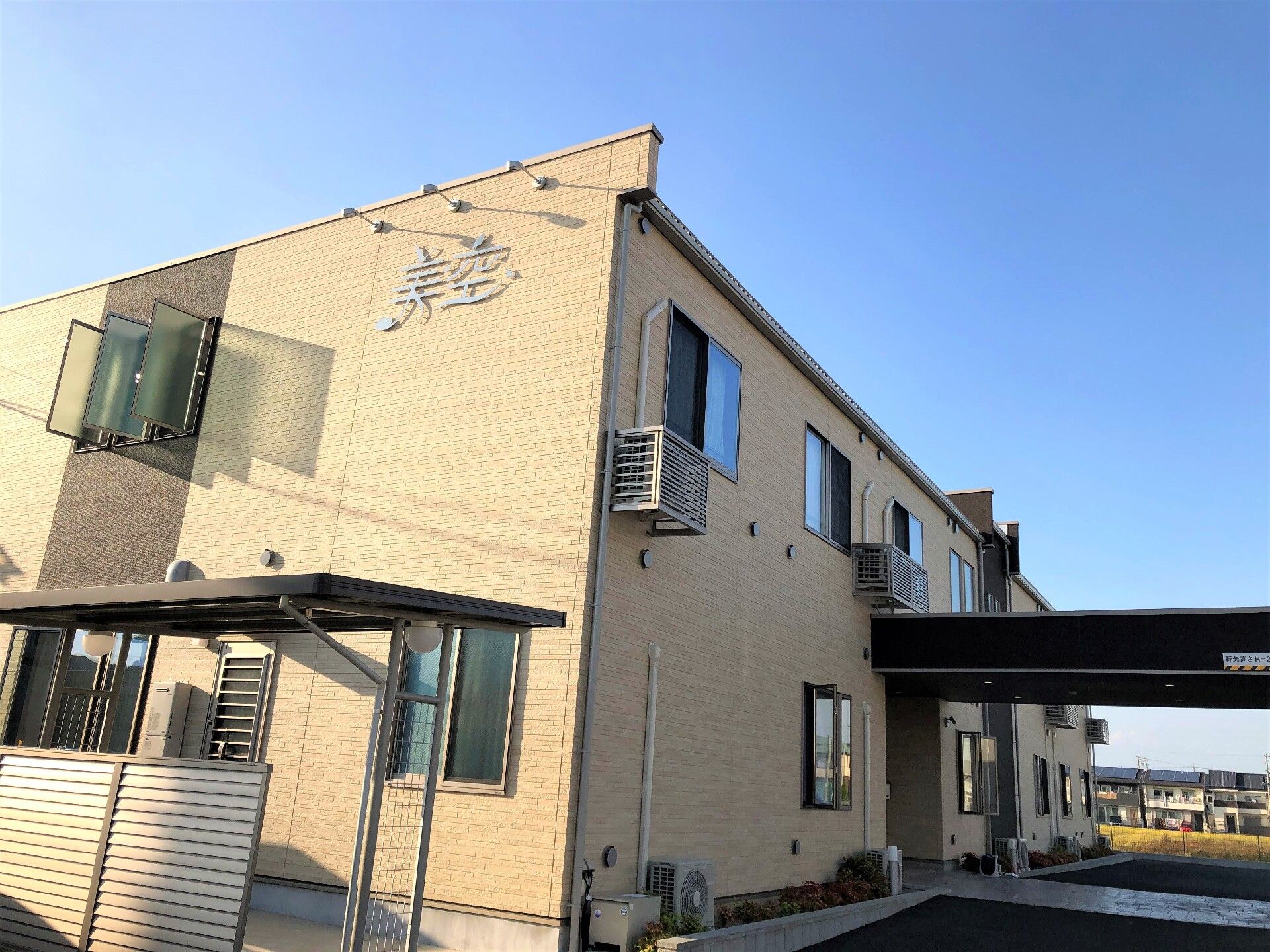 非常階段や車寄せを完備している2階建ての施設である。各居室に設置されているエアコンの室外機が見える。