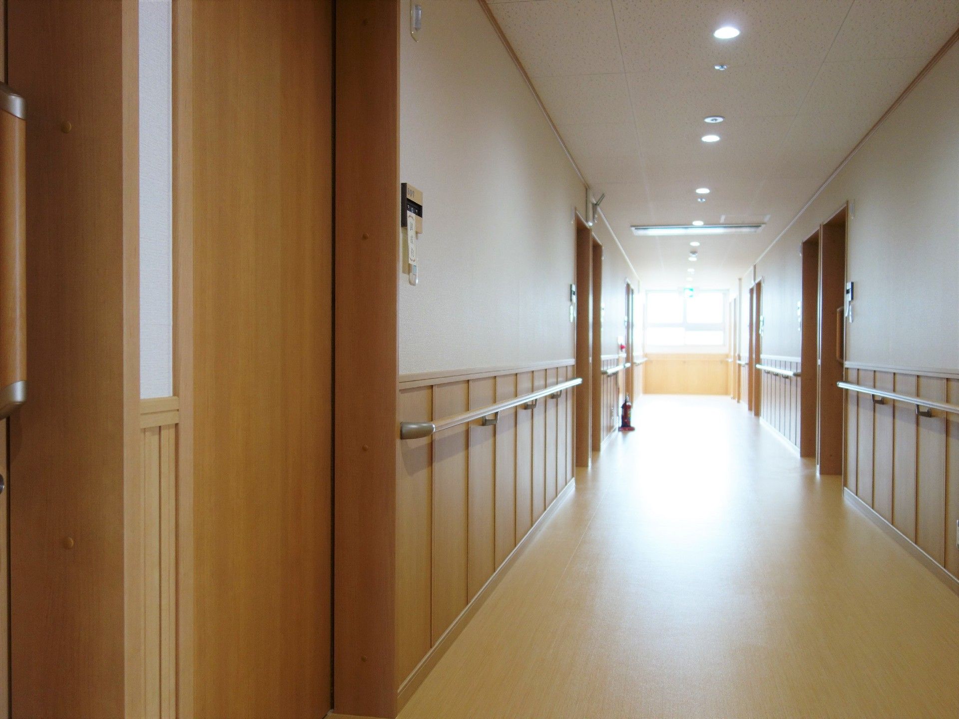 まっすぐな廊下。入居者がわかりやすいよう居室のドアと手すりの色を変えている。一番奥には大きな窓があり明るい。