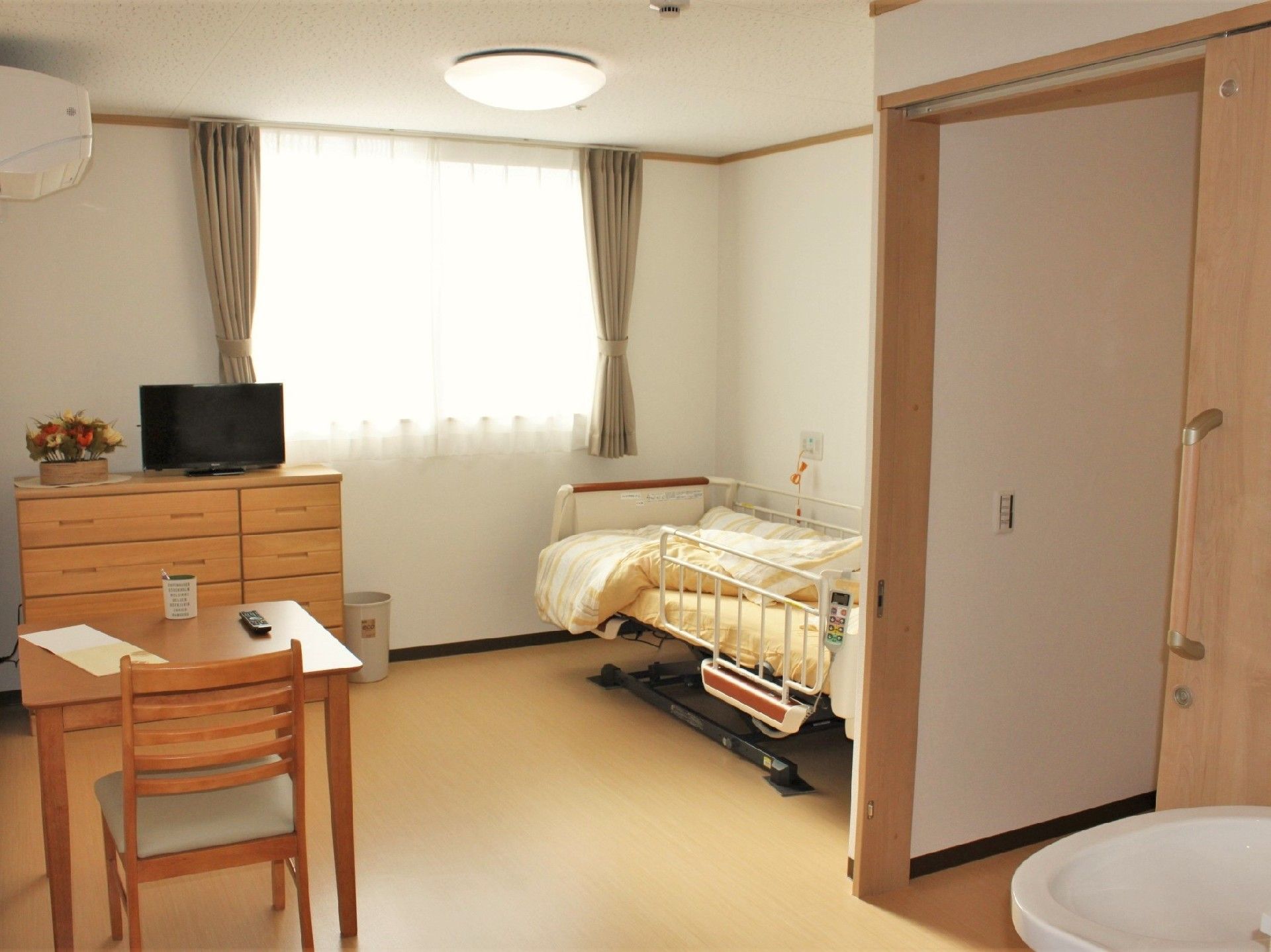 窓が輪から見渡した居室内。左にはベッドと洗面所、そして居室ドアを入ってウすぐトイレがある。