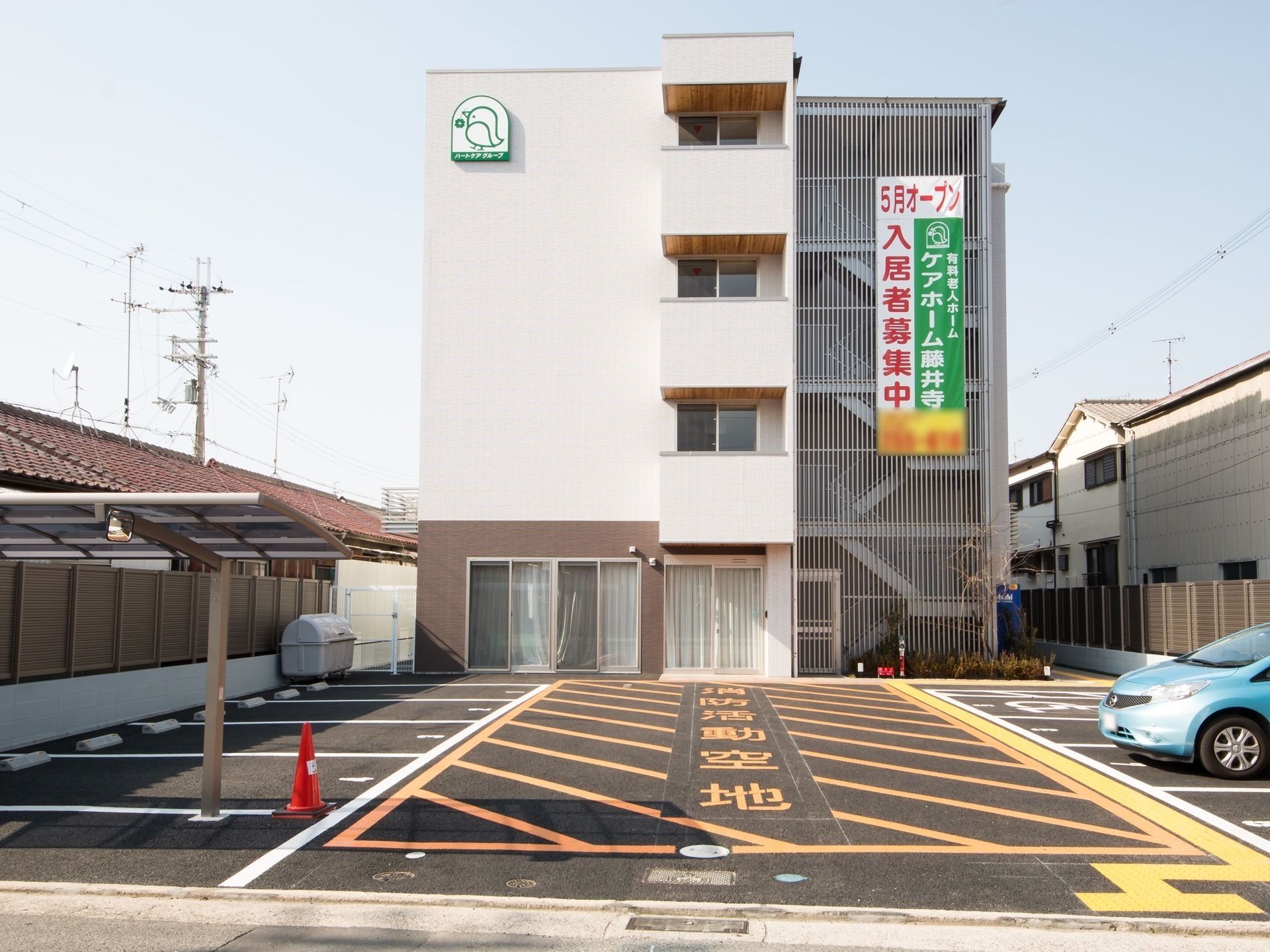 白とグレーのすっきりとした印象の建物。建物の周辺には駐車場があり、人が行き来している様子が見える。
