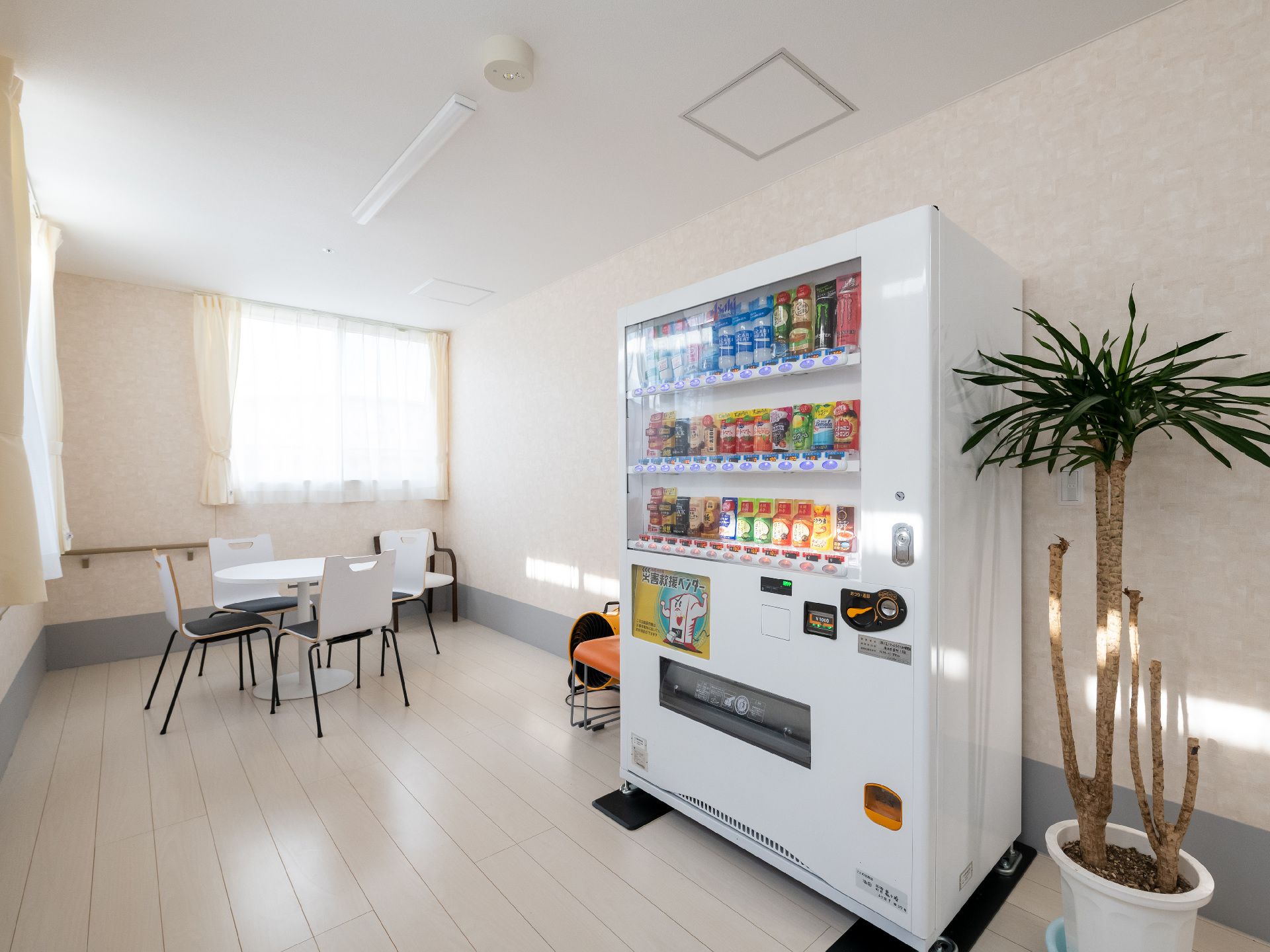 白い自販機の奥にテーブルと椅子がおかれている共有スペース