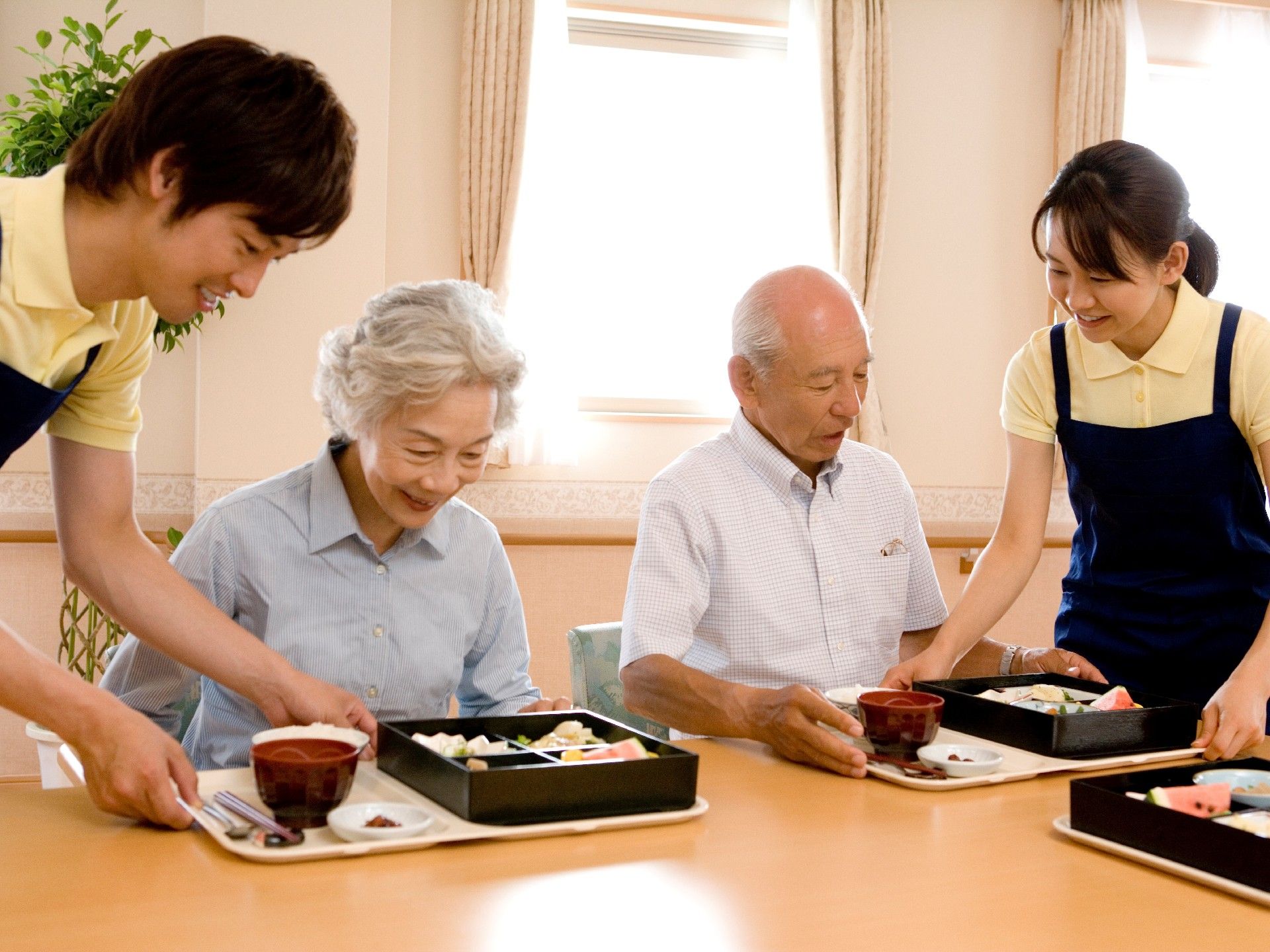 夫婦の入居者に食事が提供されている様子。ポロシャツの上にエプロンをつけたスタッフが対応している。
