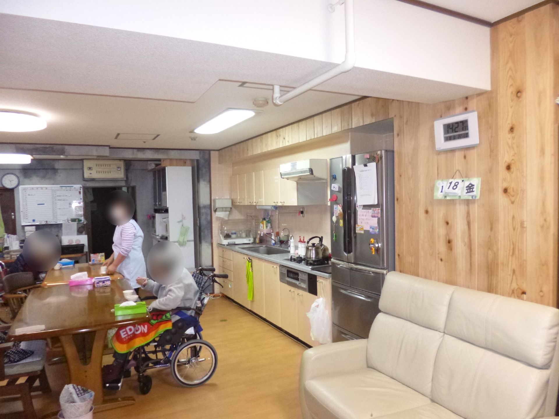 木目調を生かした壁に家庭と同じようなサイズのキッチン、中央にはテーブルが置かれ、入居者やスタッフがいる。
