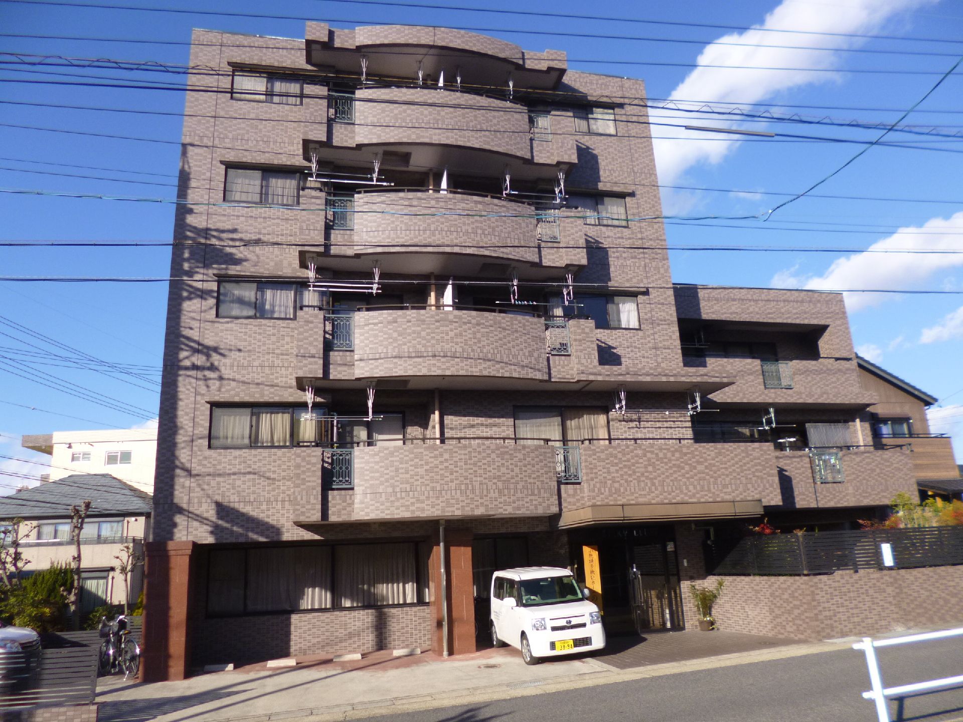 ブラウンを基調とした外観。玄関先には屋根が付き、建物1階部分には駐車スペースがある。